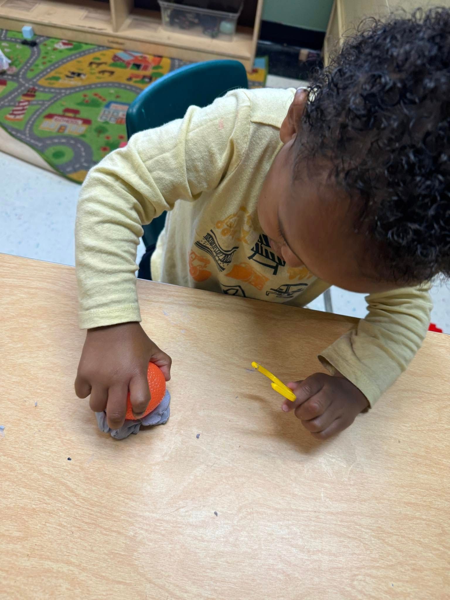 A young girl is sitting at a table playing with clay.
