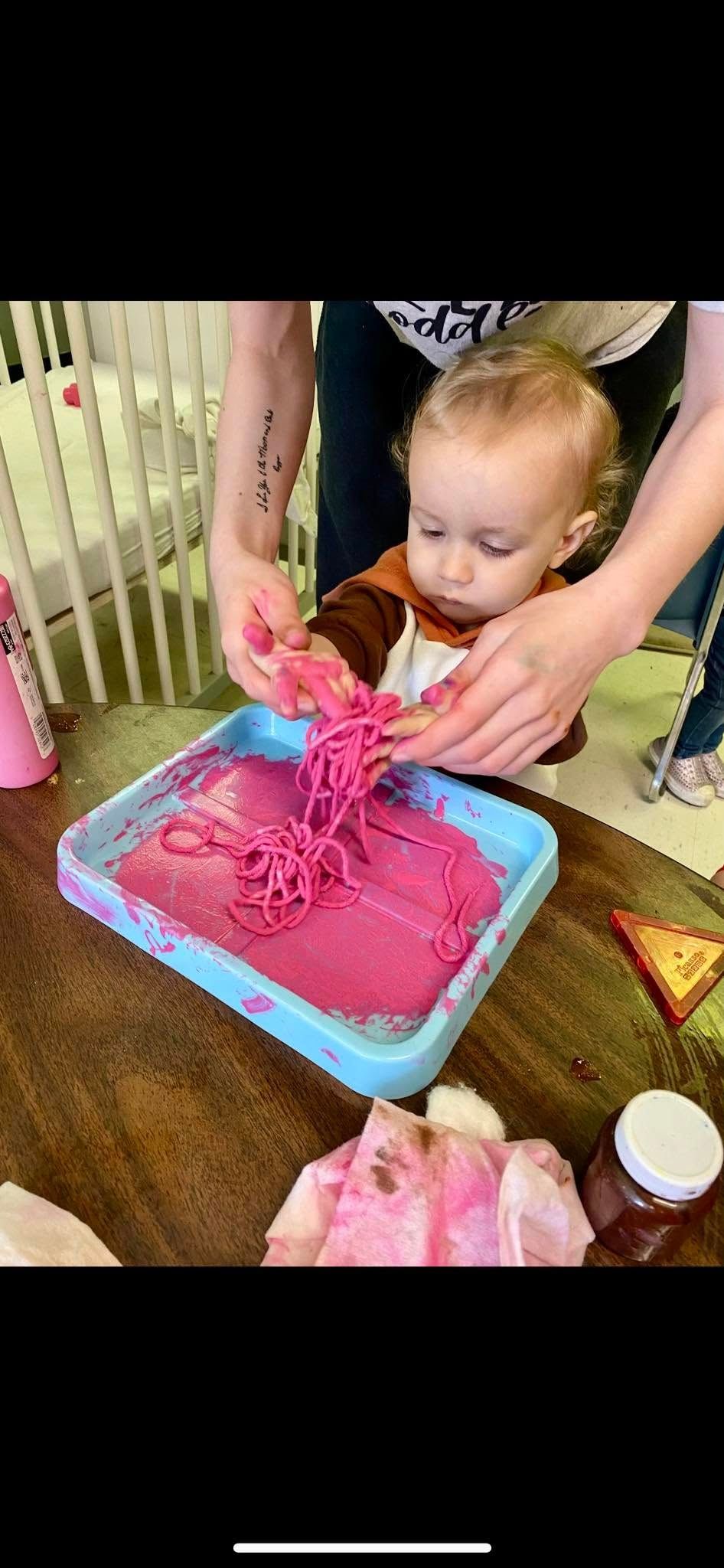 A baby is playing with pink sand on a table.