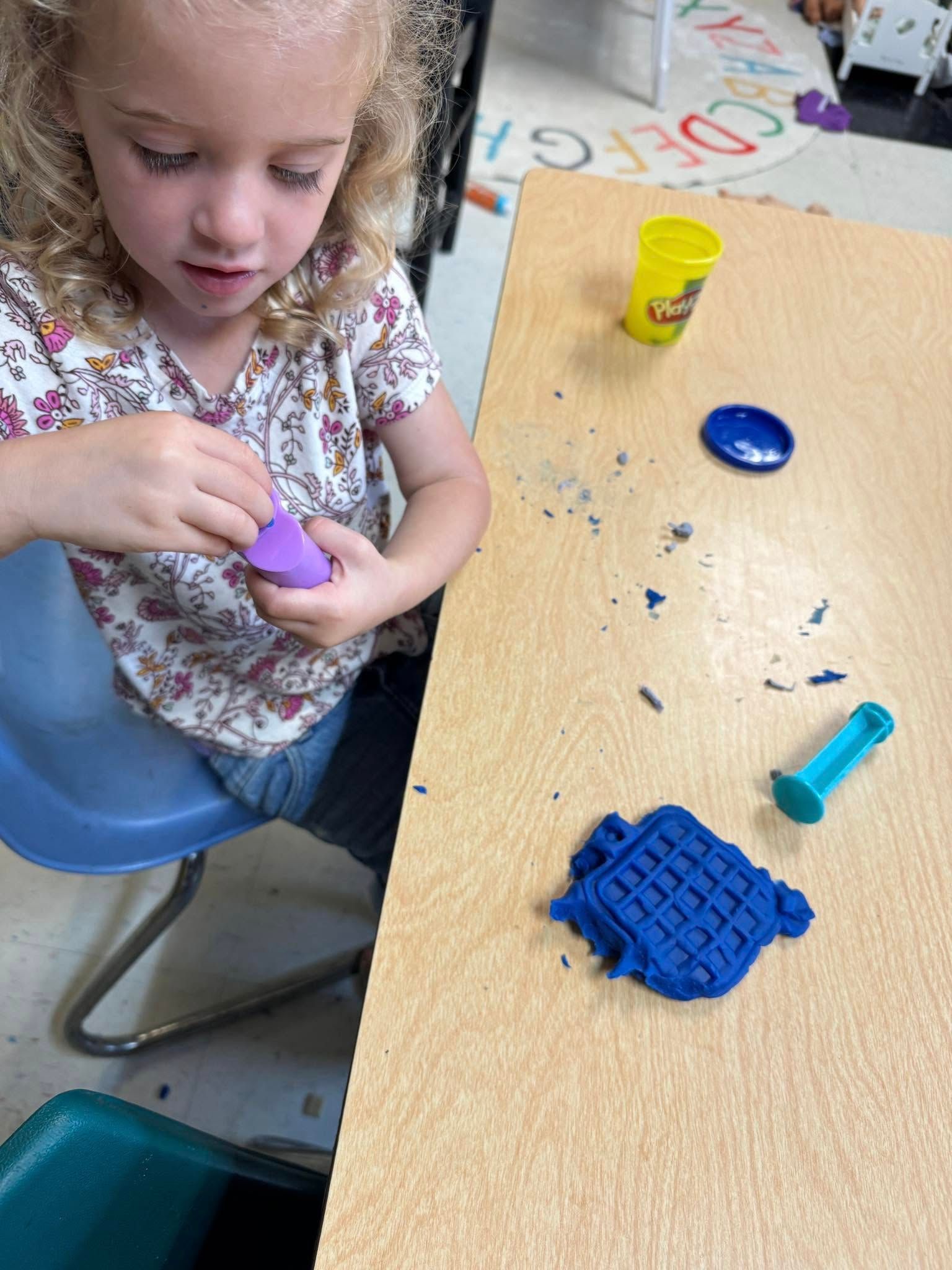 A little girl is sitting at a table playing with play dough.