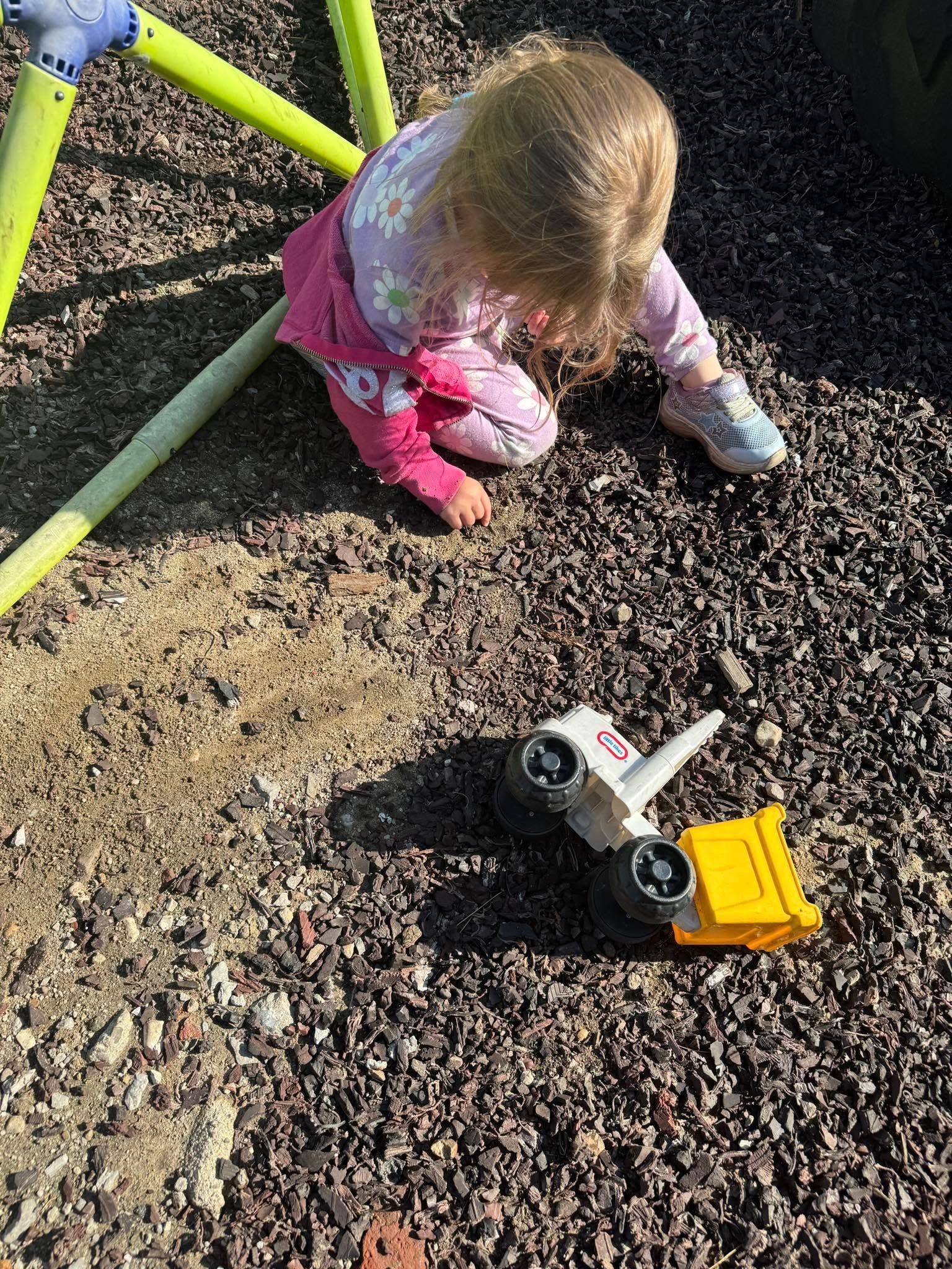A little girl is playing with a toy truck on the ground.