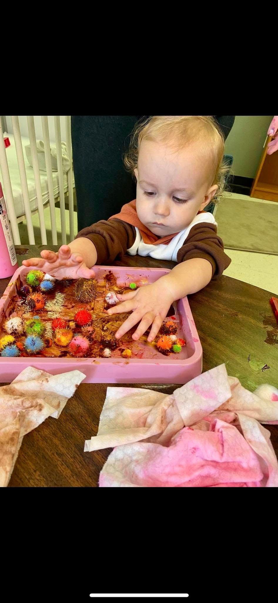 A baby is playing with a pink tray of food.