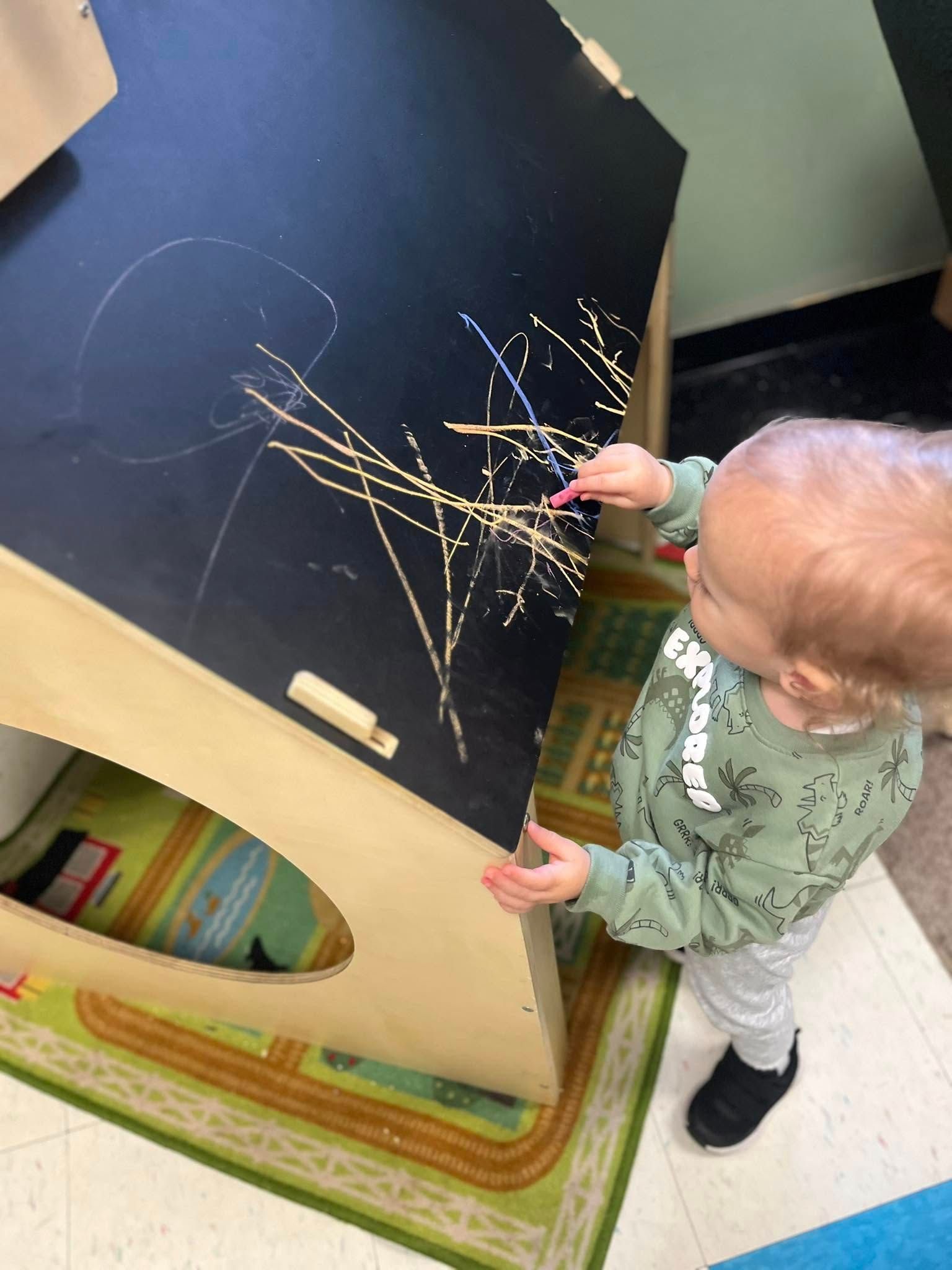 A baby is playing with sticks on a blackboard.