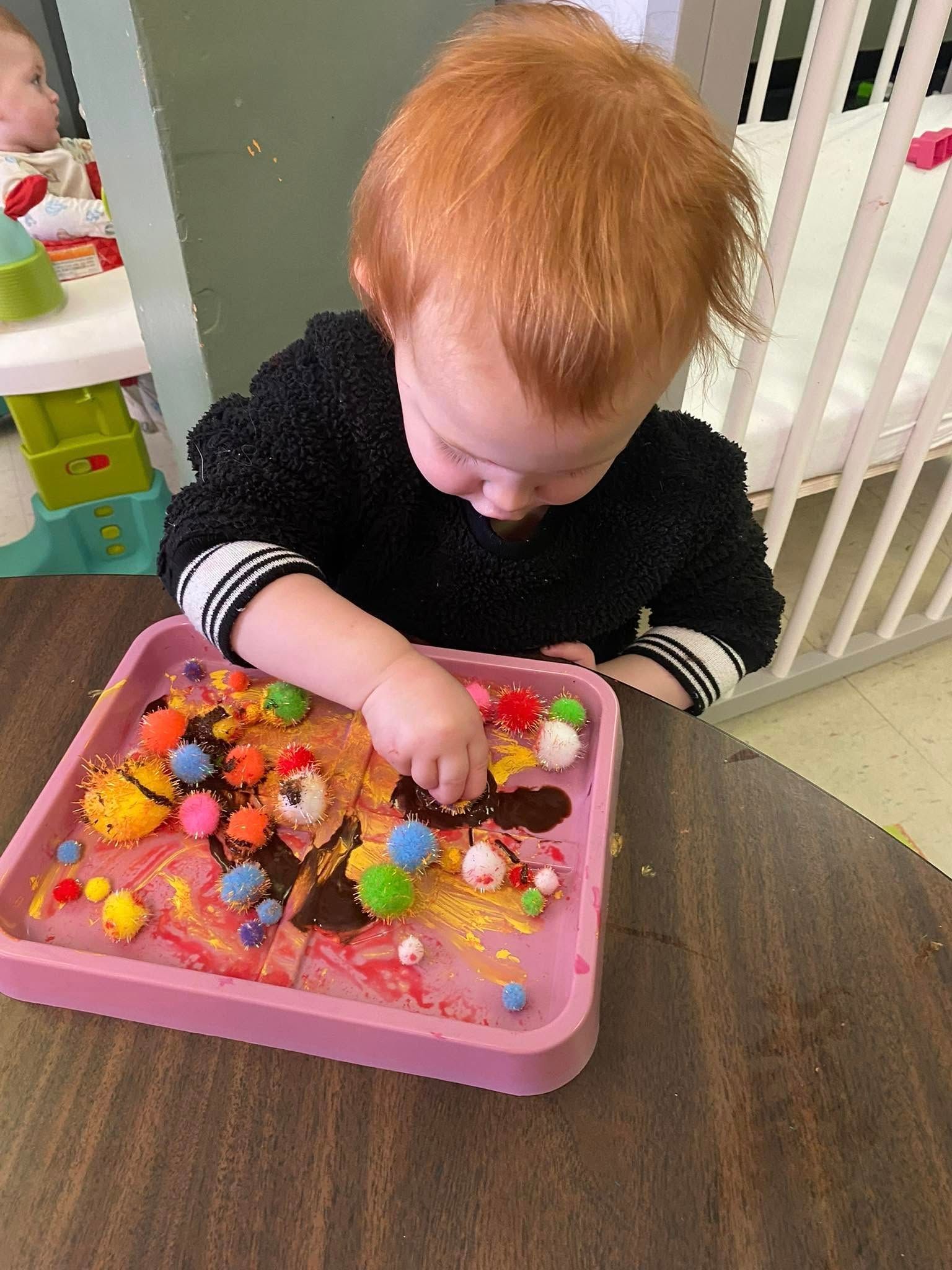 A baby is playing with a pink tray of toys on a table.