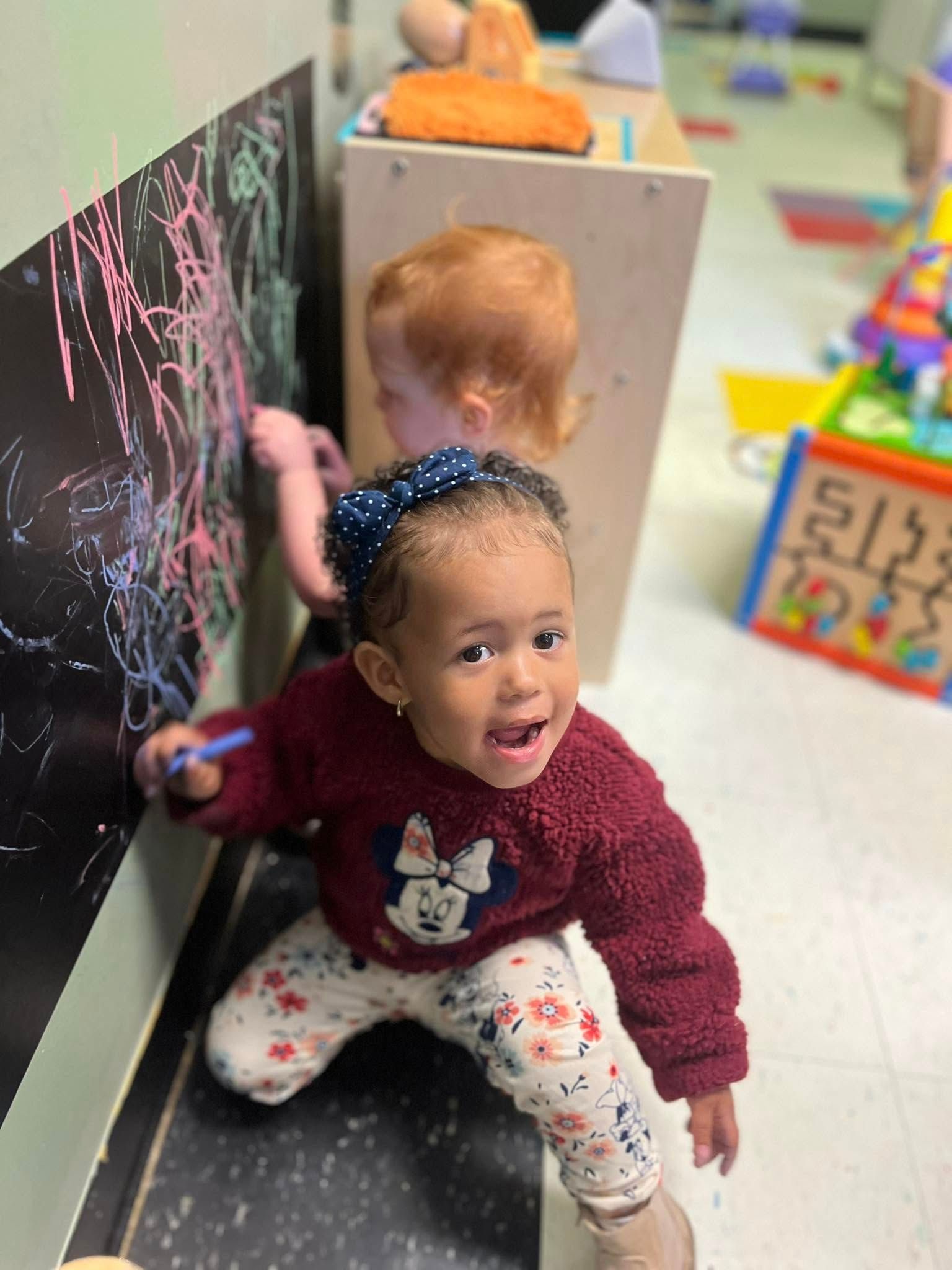 A little girl is sitting on the floor drawing on a blackboard.
