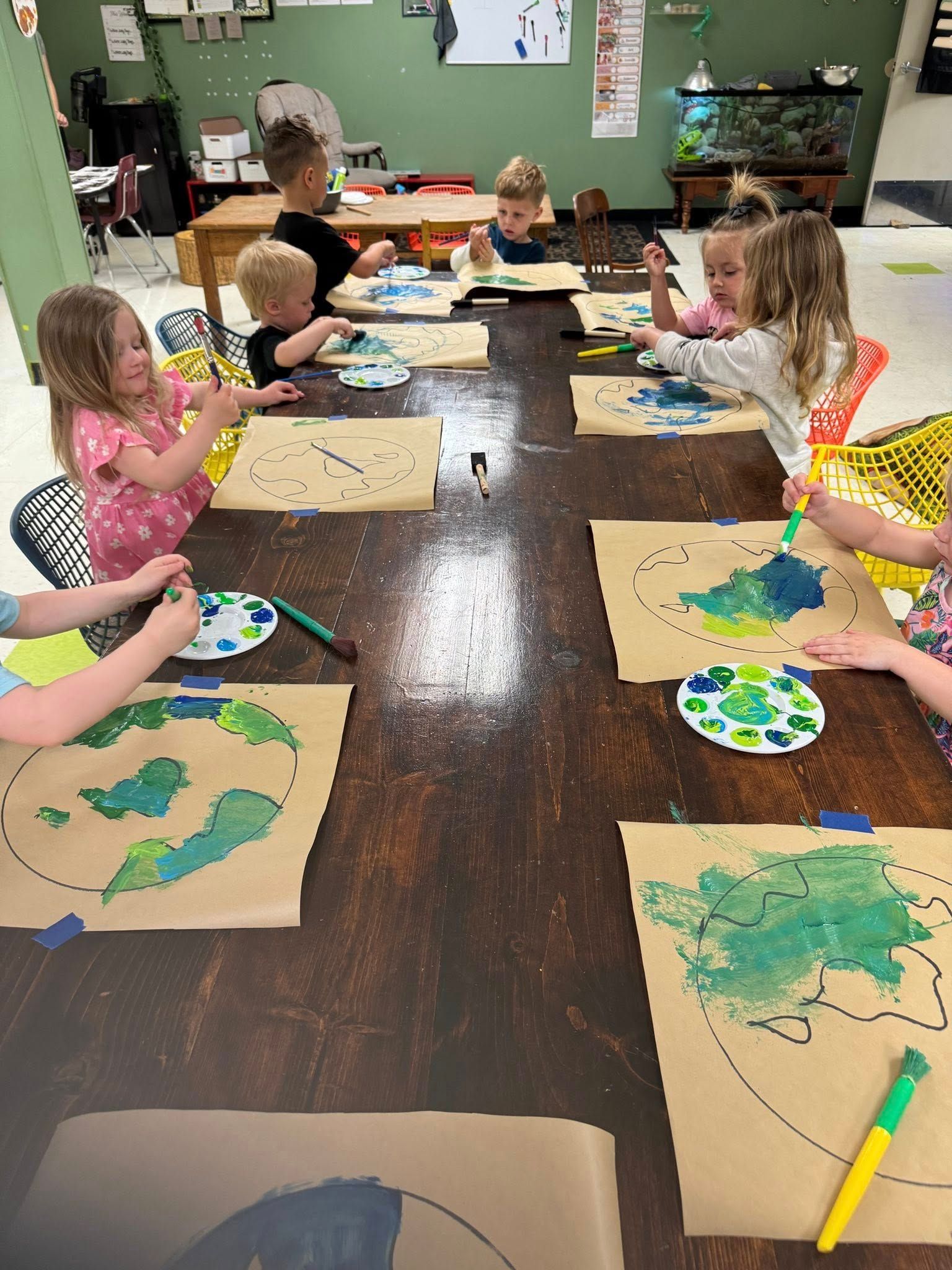 A group of children are sitting at a table painting.