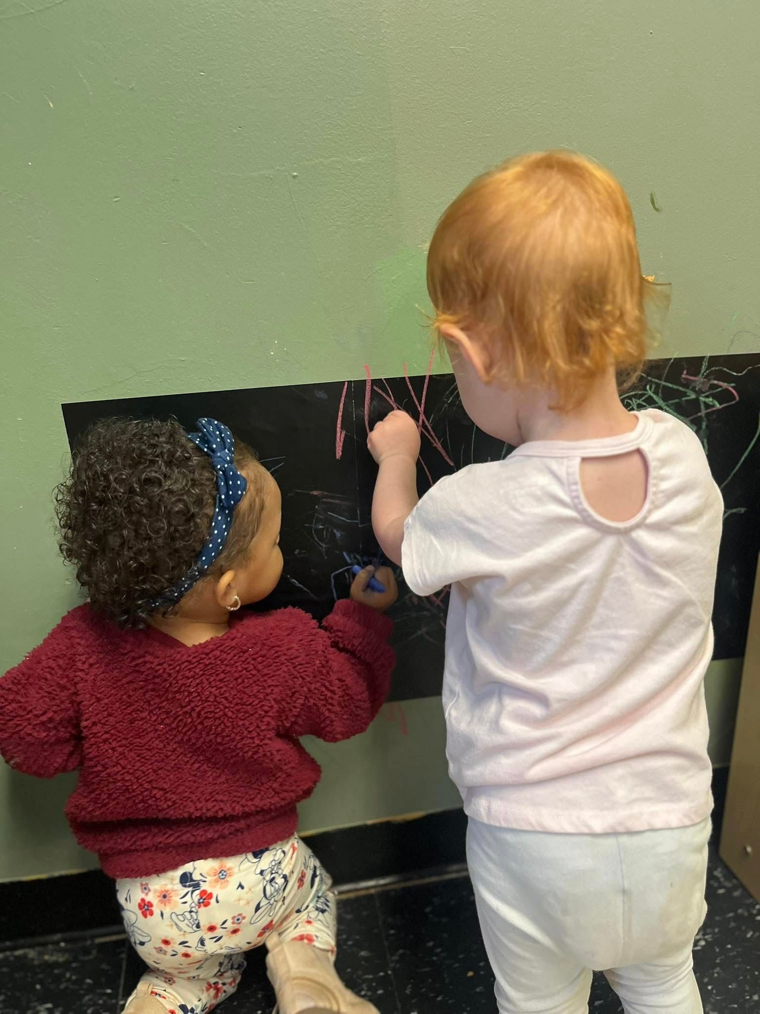 Two little girls are drawing on a blackboard.