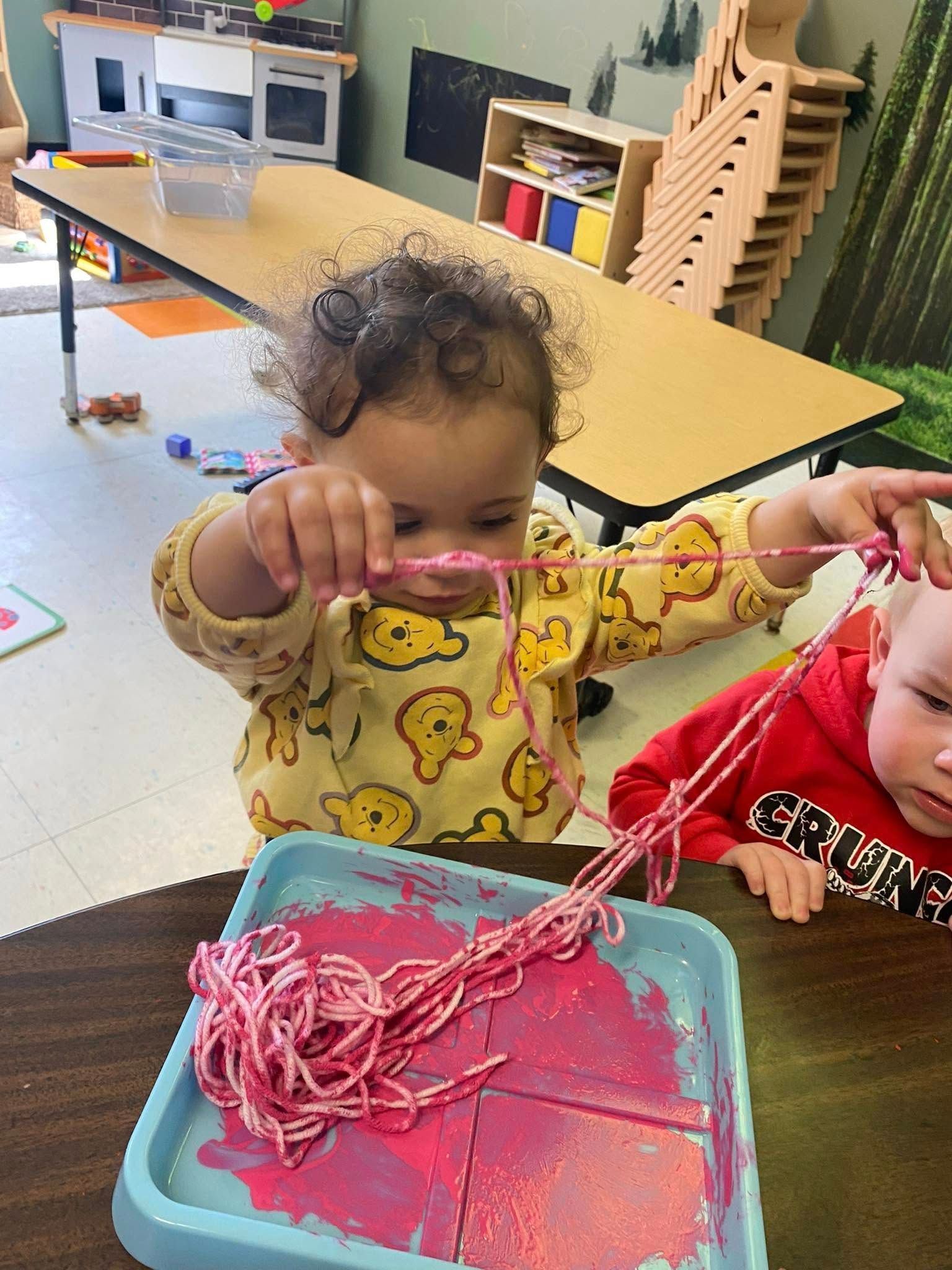 A little girl is playing with pink paint on a table.