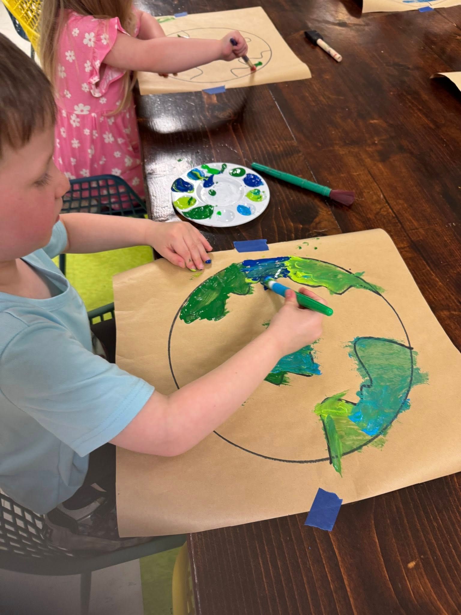 A boy and a girl are painting a globe on a piece of paper.
