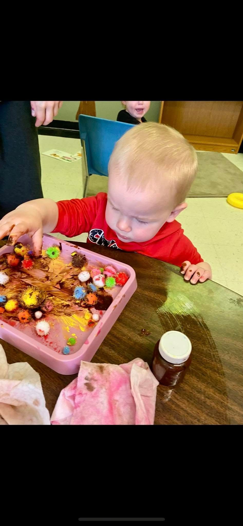 A baby is playing with a tray of candy on a table.