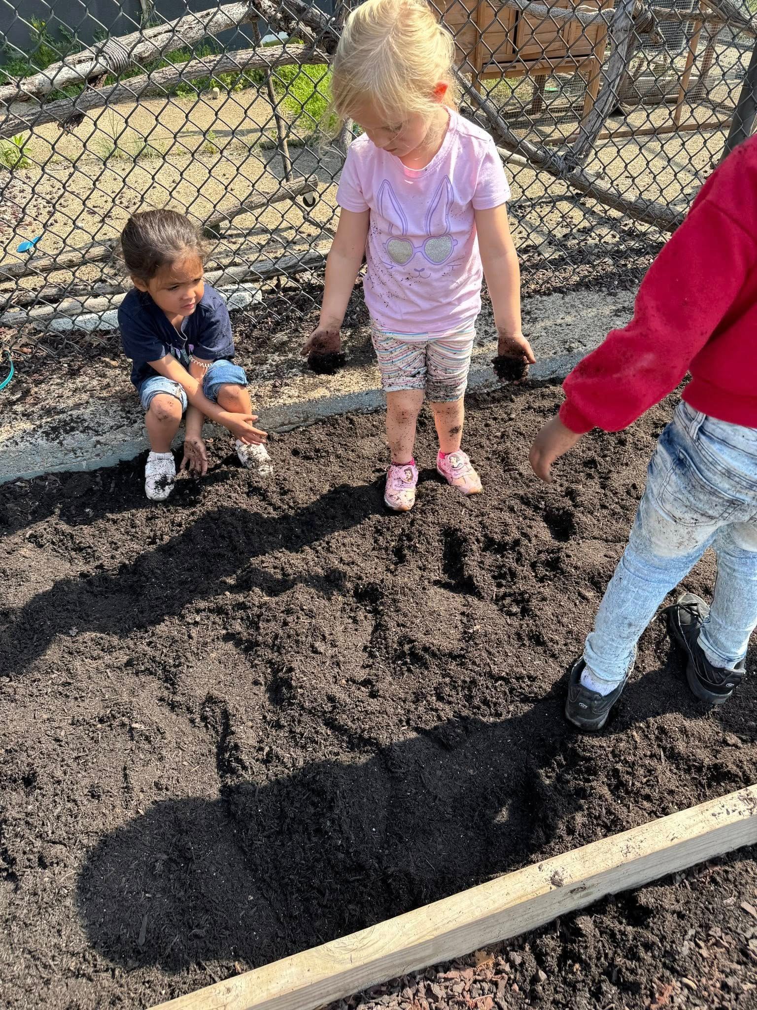 Two young children are playing in the dirt in a garden.
