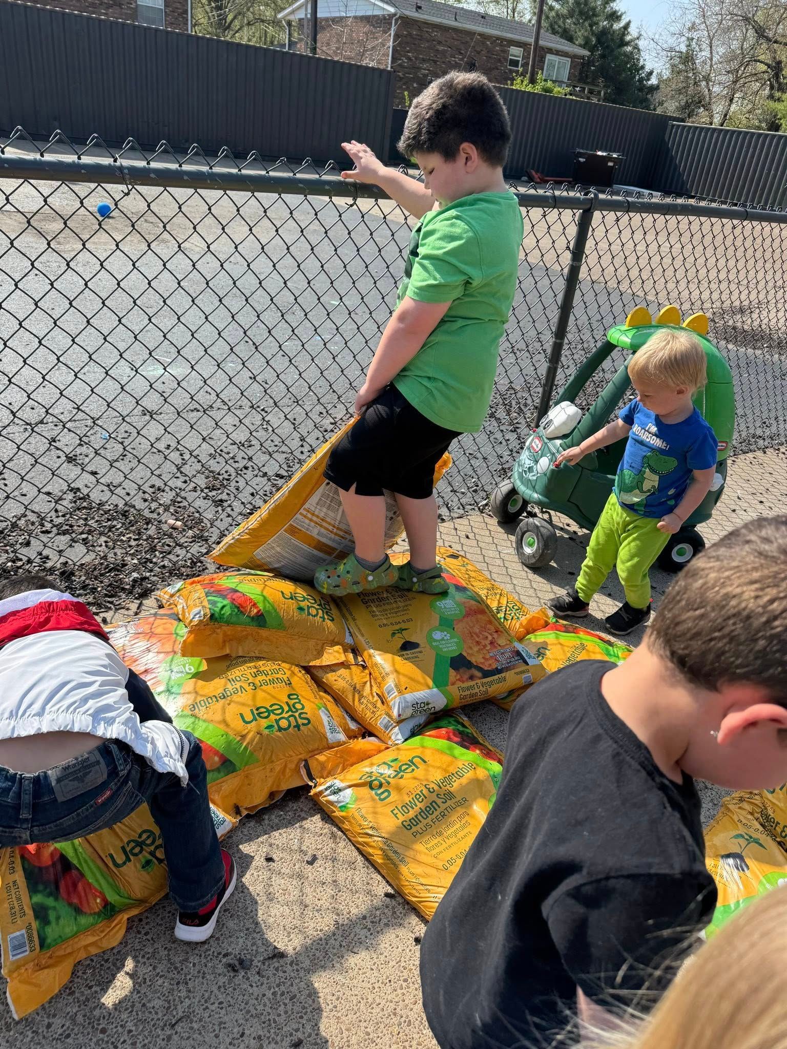 A group of children are standing around a pile of bags of dirt.