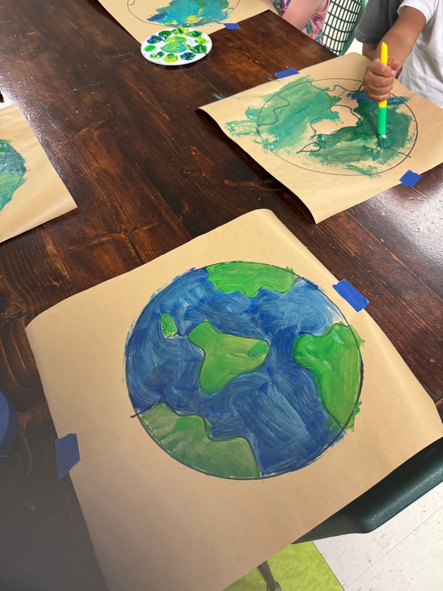 A child is painting a picture of the earth on a piece of brown paper.