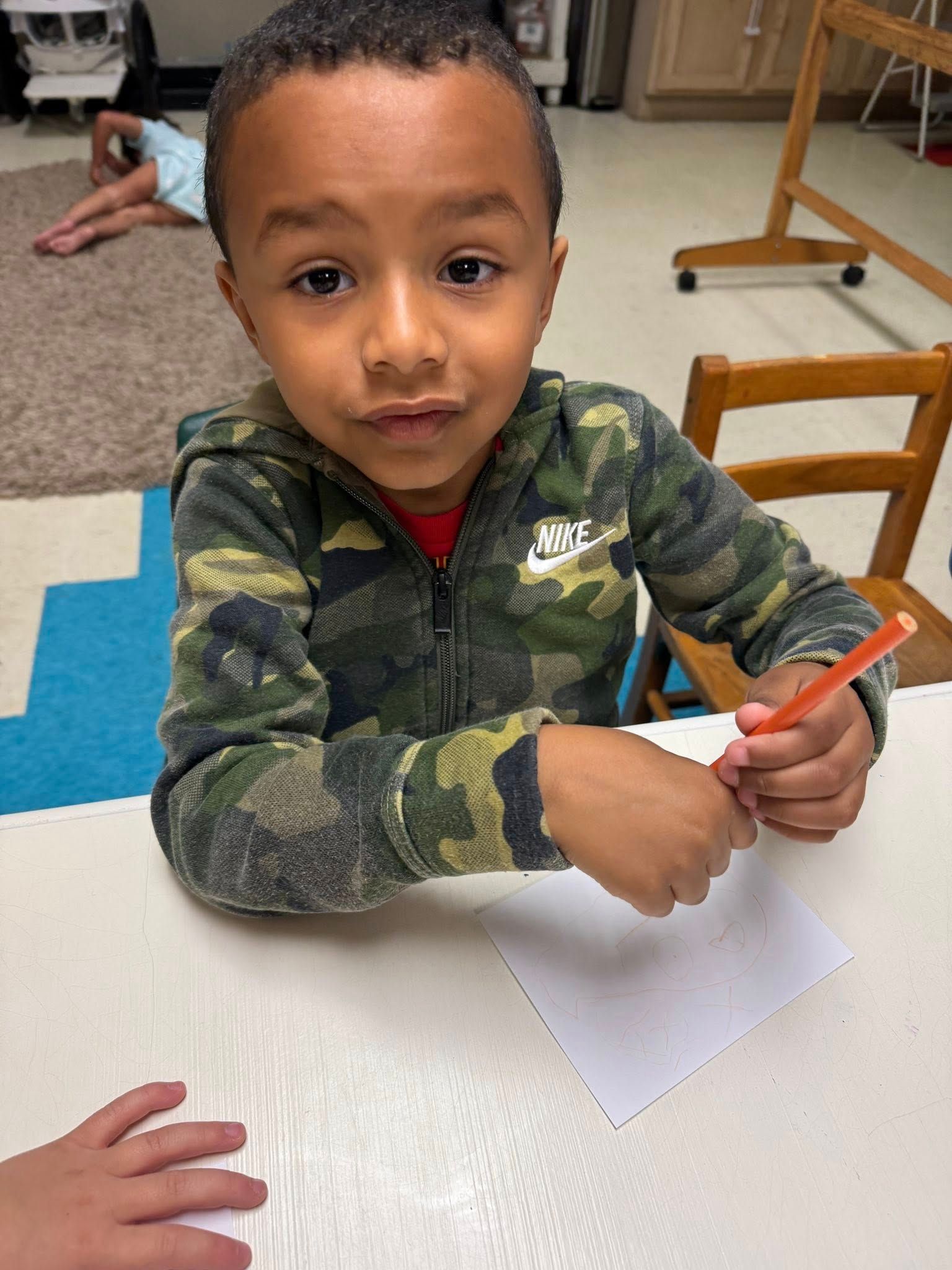 A young boy is sitting at a table holding a pencil.