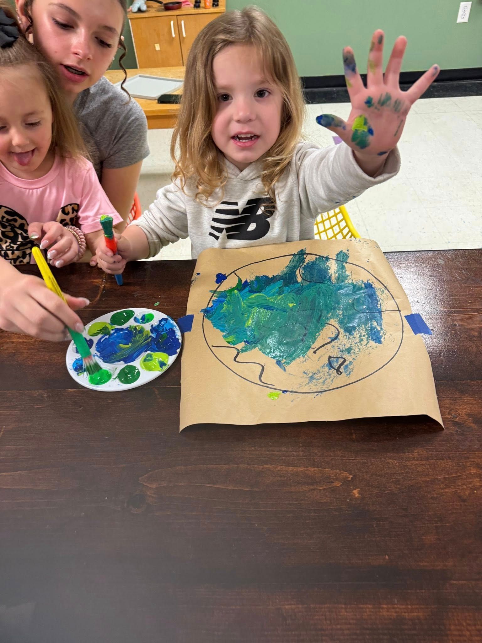Two little girls are sitting at a table painting with their hands.