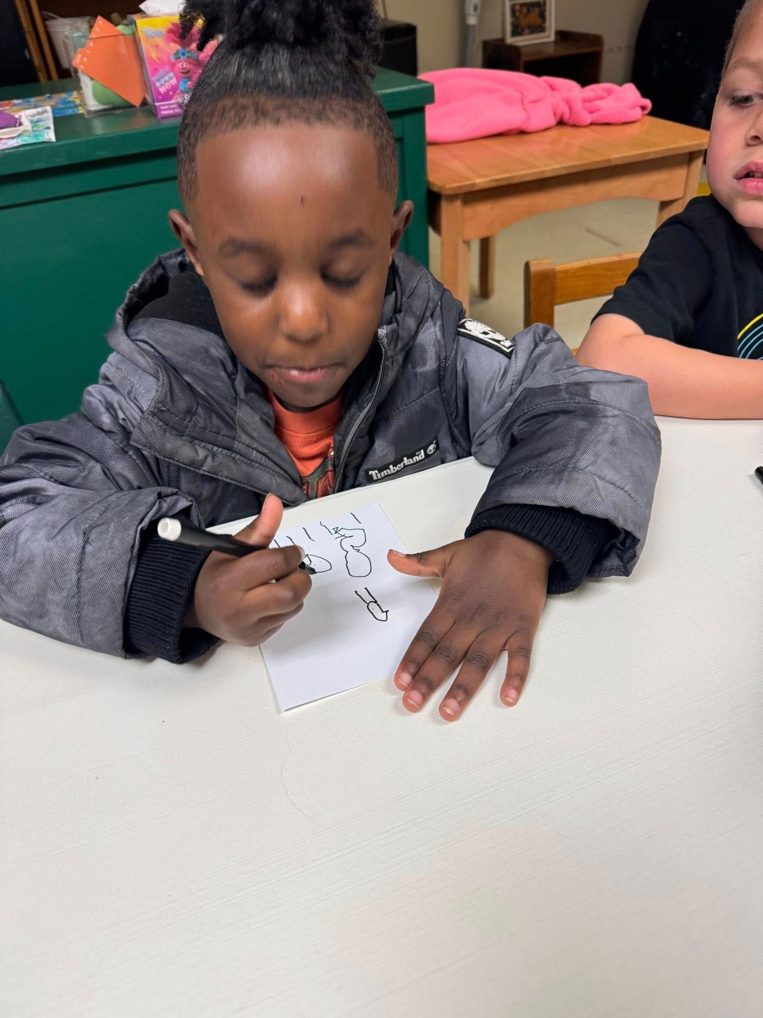 A young boy is sitting at a table writing on a piece of paper.