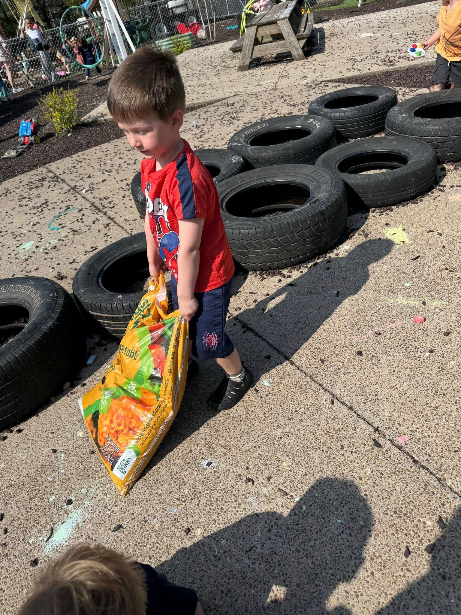 A young boy is pushing a bag of dirt on a tire track.