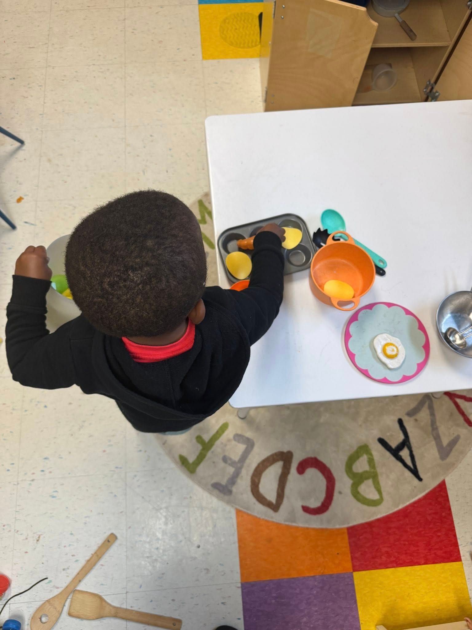A child is playing with a toy kitchen set on a rug that says abcdef