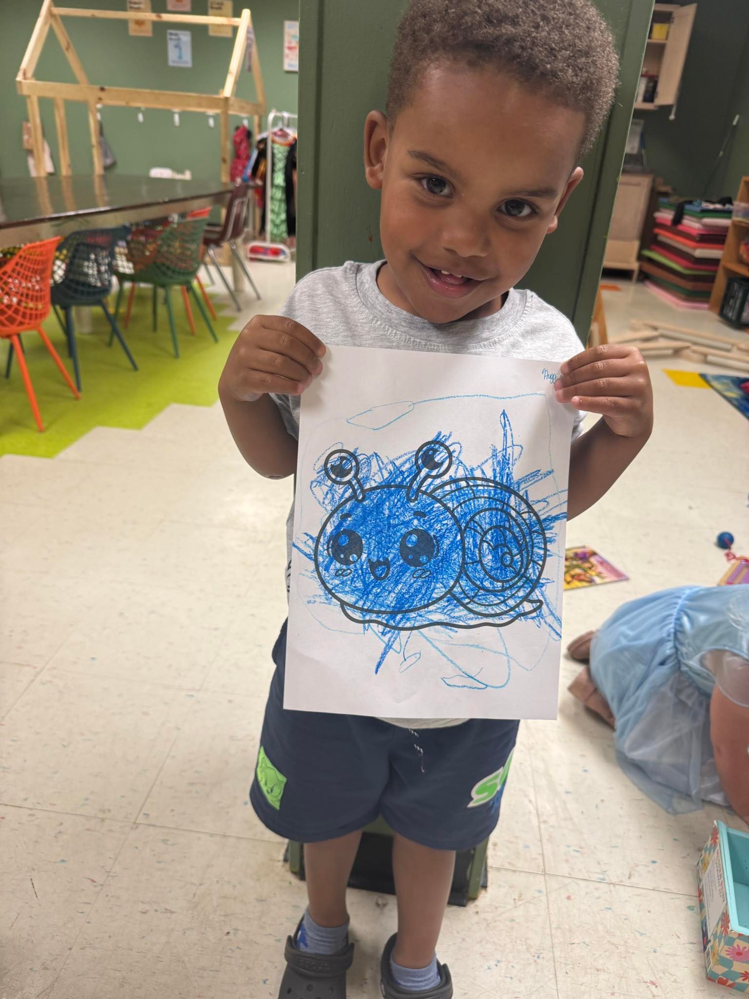 A young boy is holding up a drawing of a blue cloud.