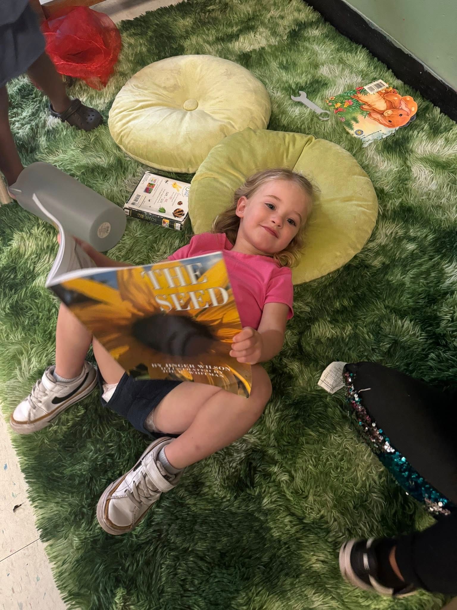 A young girl laying on her back reading The Seed