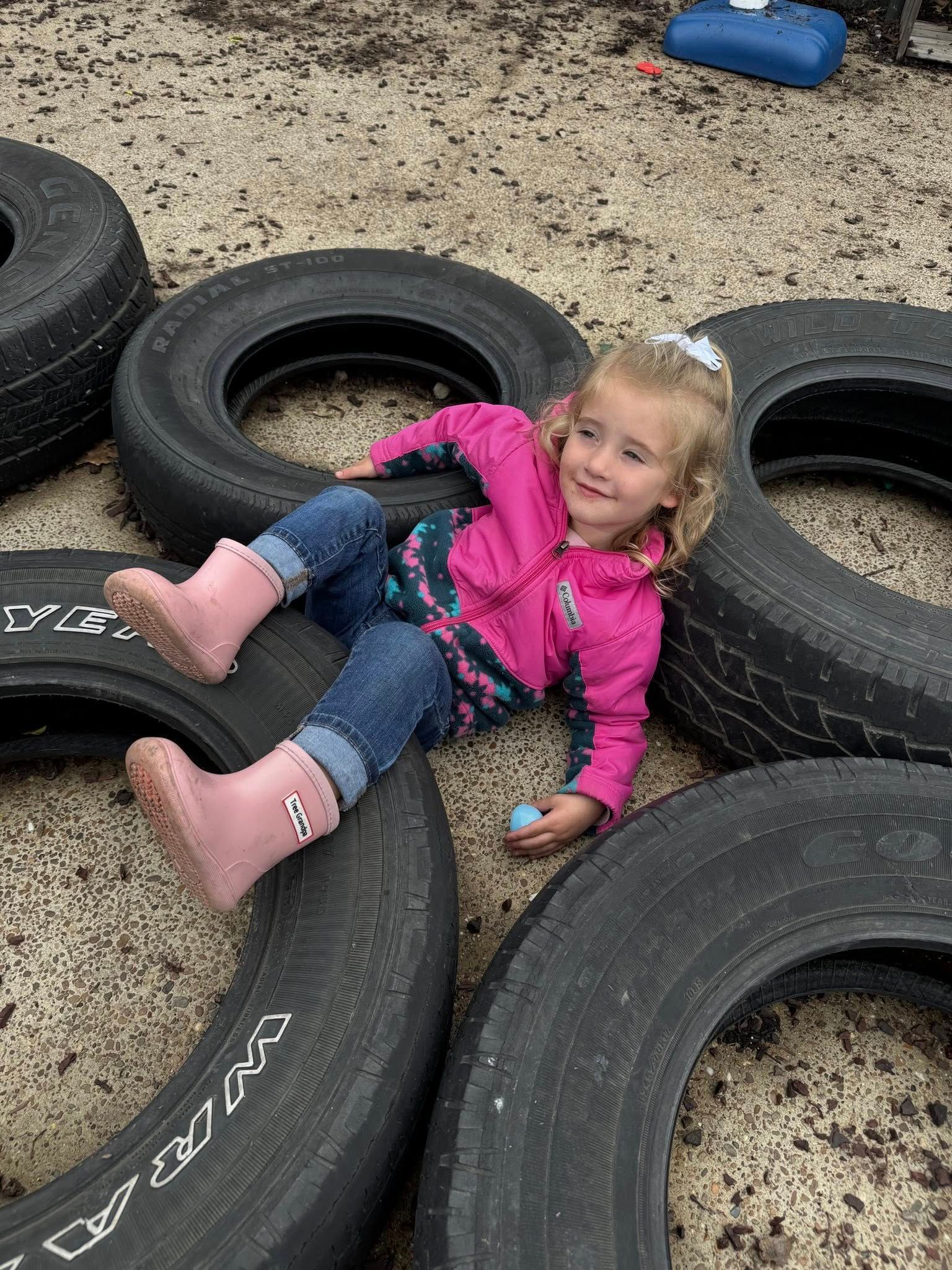 A little girl is laying on top of a pile of tires.