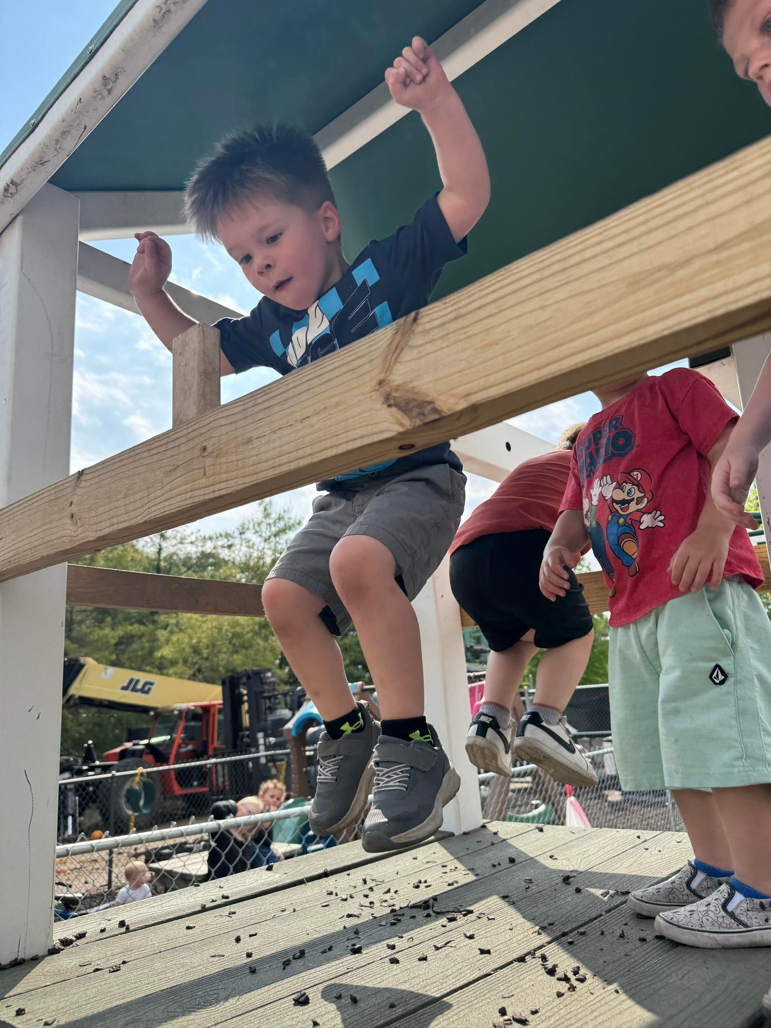 A young boy is jumping over a wooden beam.