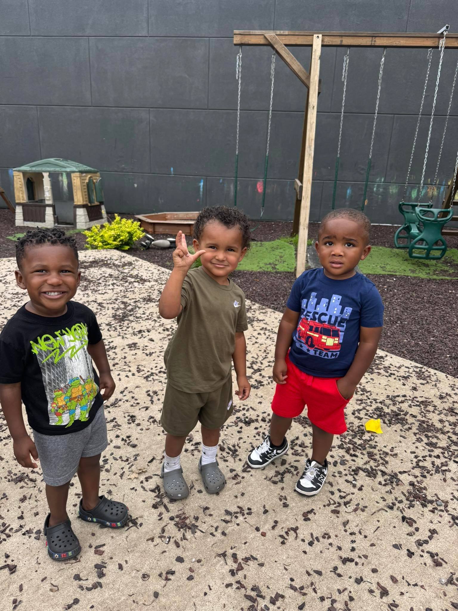 Three young boys are standing next to each other in a sandbox.