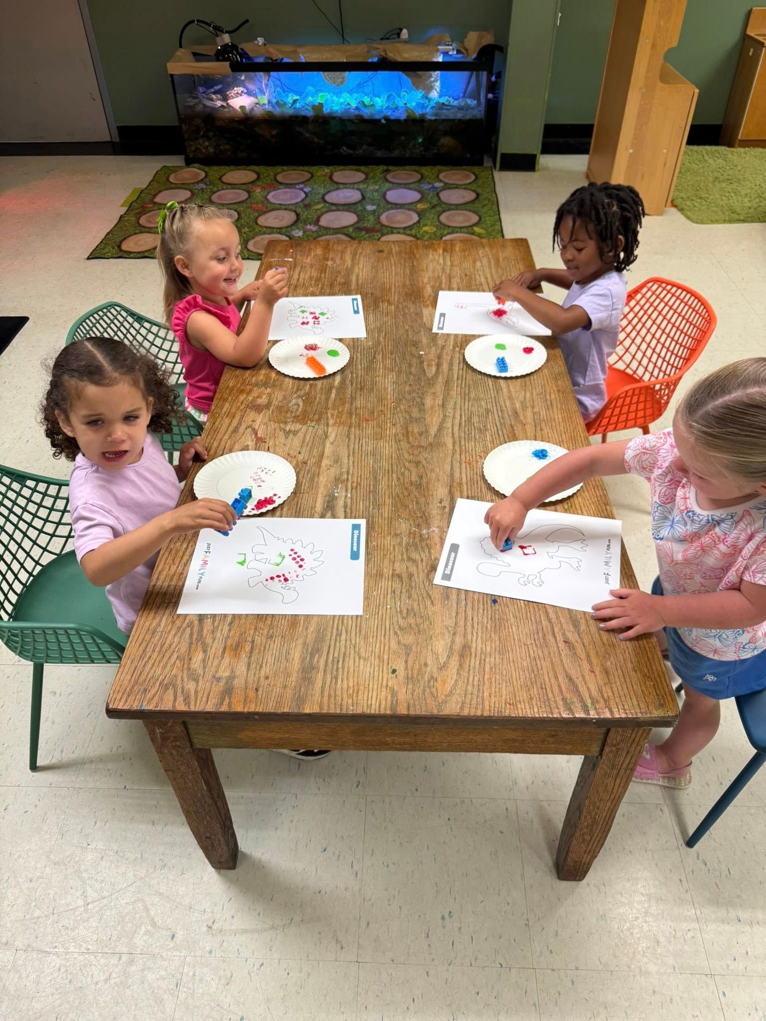 A group of young girls are sitting at a table painting with paper plates.