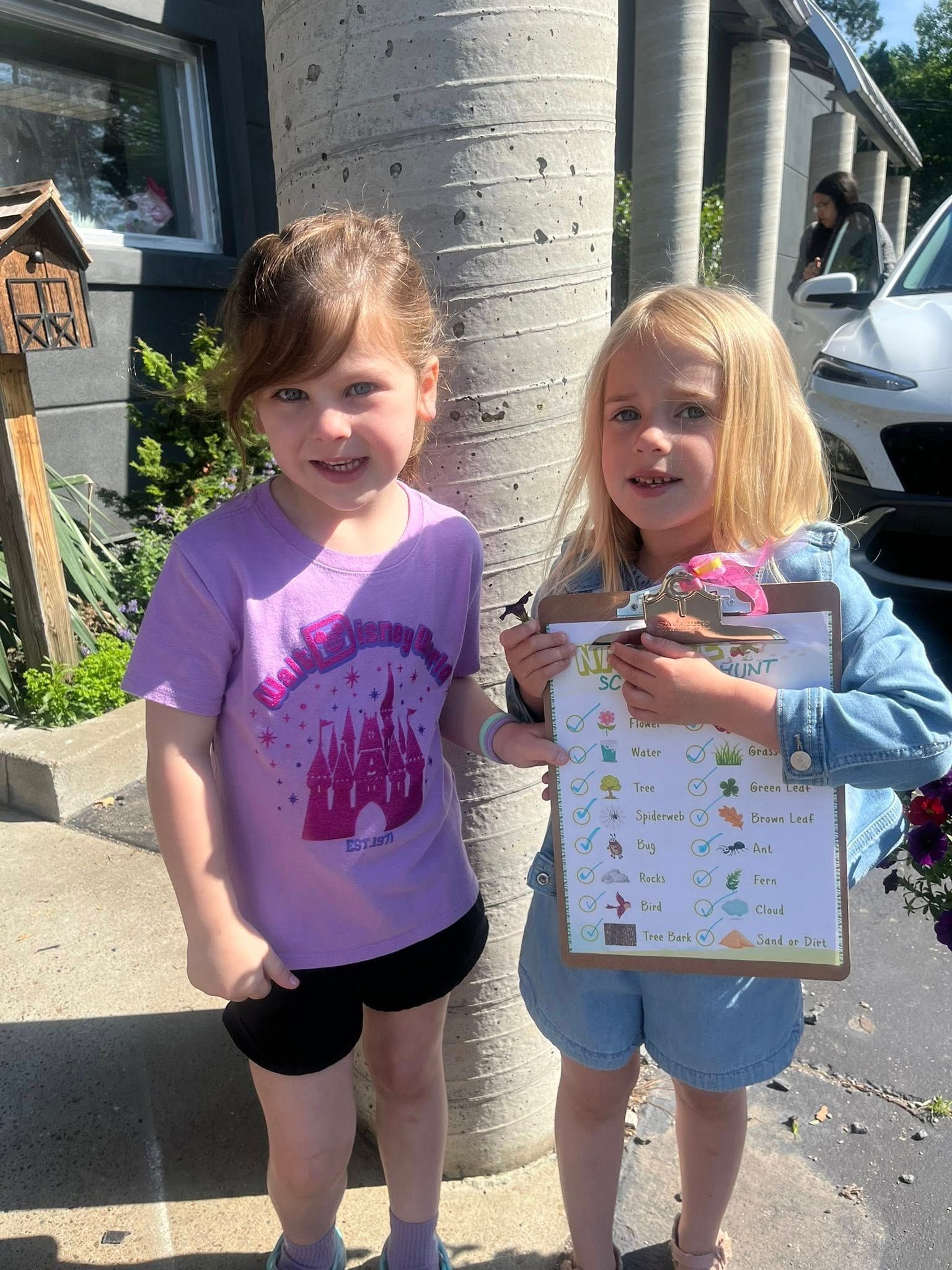 Two little girls are standing next to each other holding a clipboard.