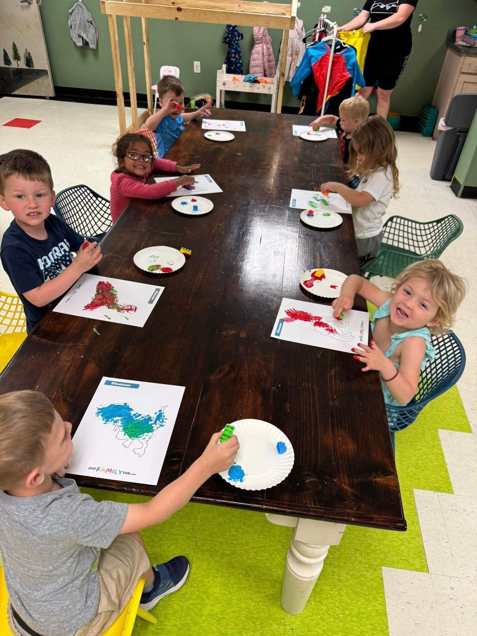 A group of children are sitting at a long table painting.