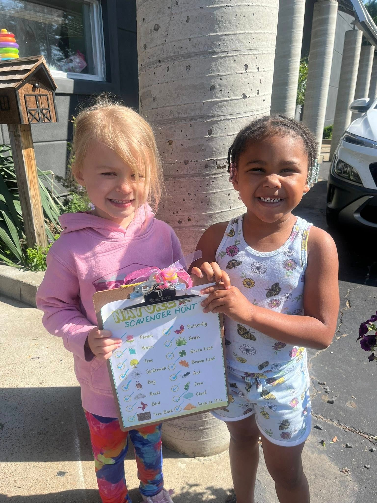 Two little girls are standing next to each other holding a clipboard.