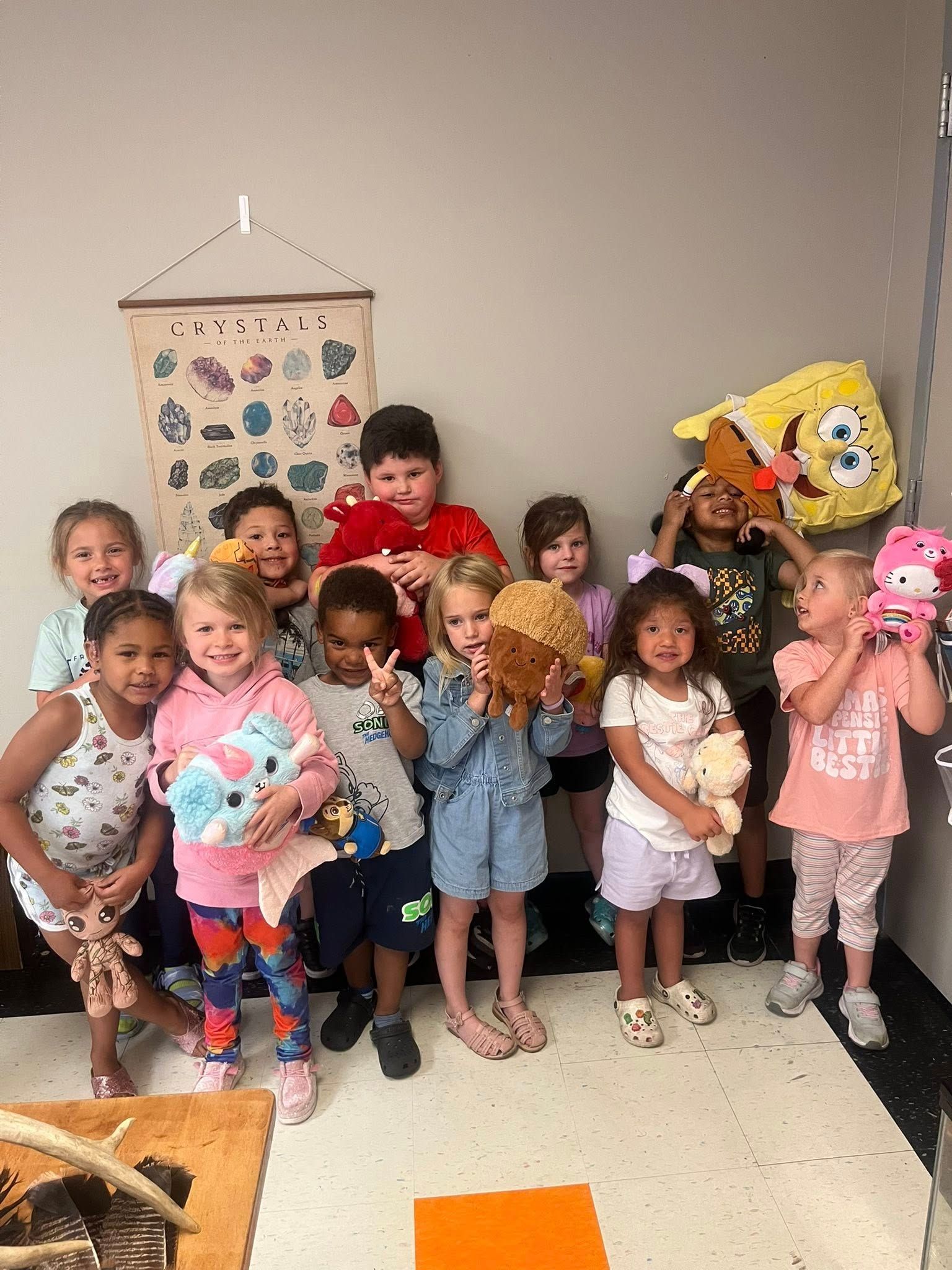 A group of children are standing next to each other in a room holding stuffed animals.