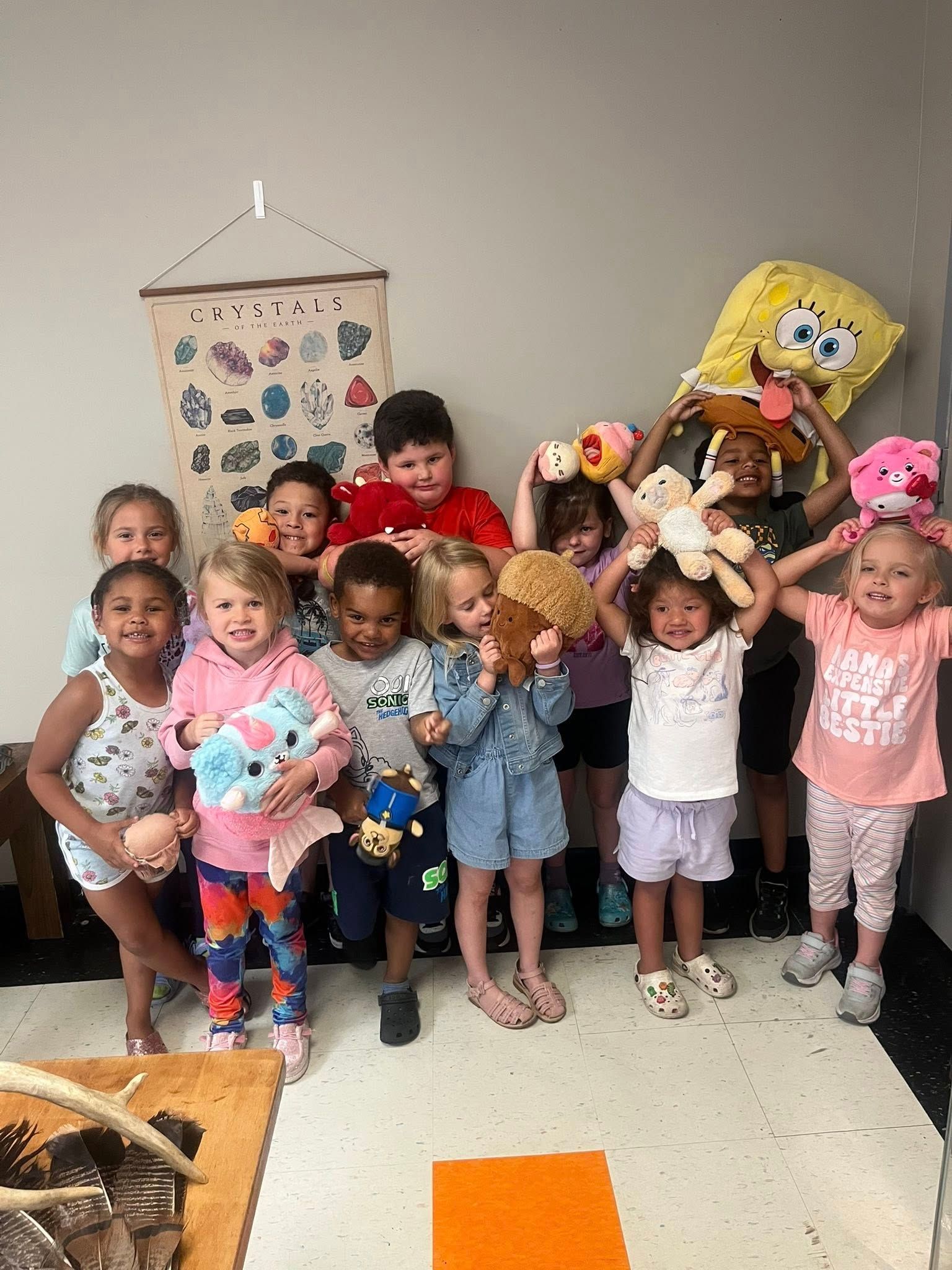 A group of children are standing in a room holding stuffed animals.