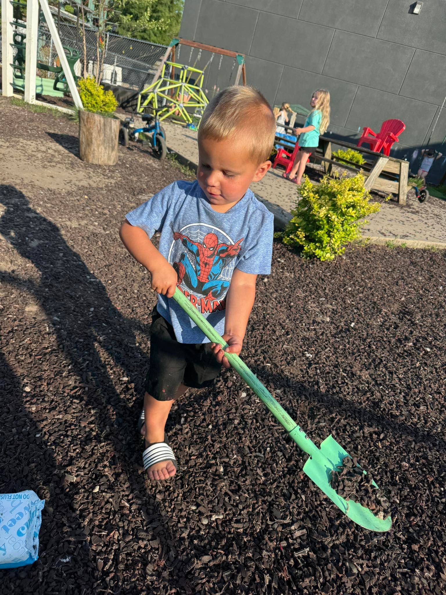 A young boy is playing with a green shovel in the dirt.