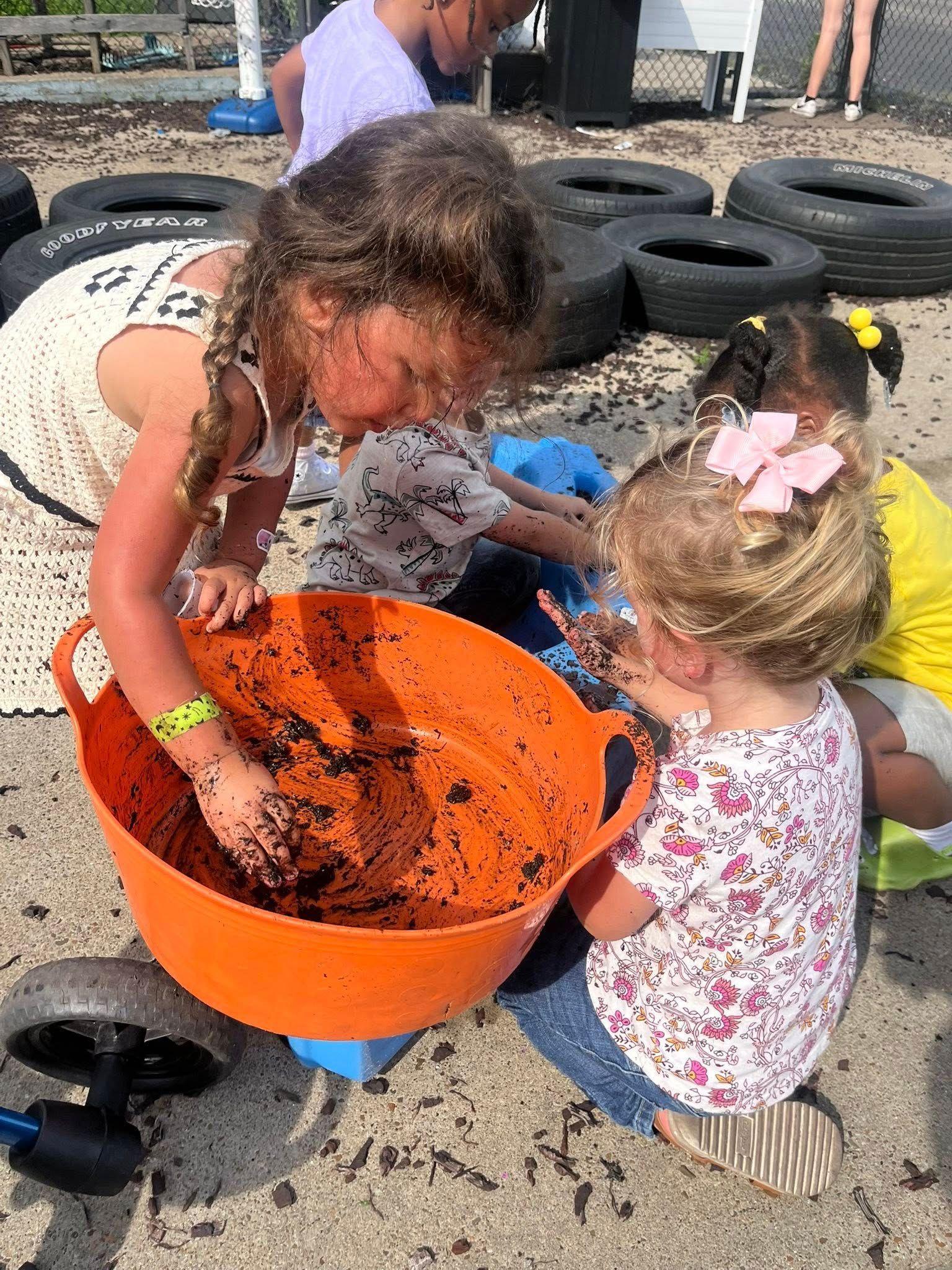 A group of young girls are playing in the sand with a large orange bucket.