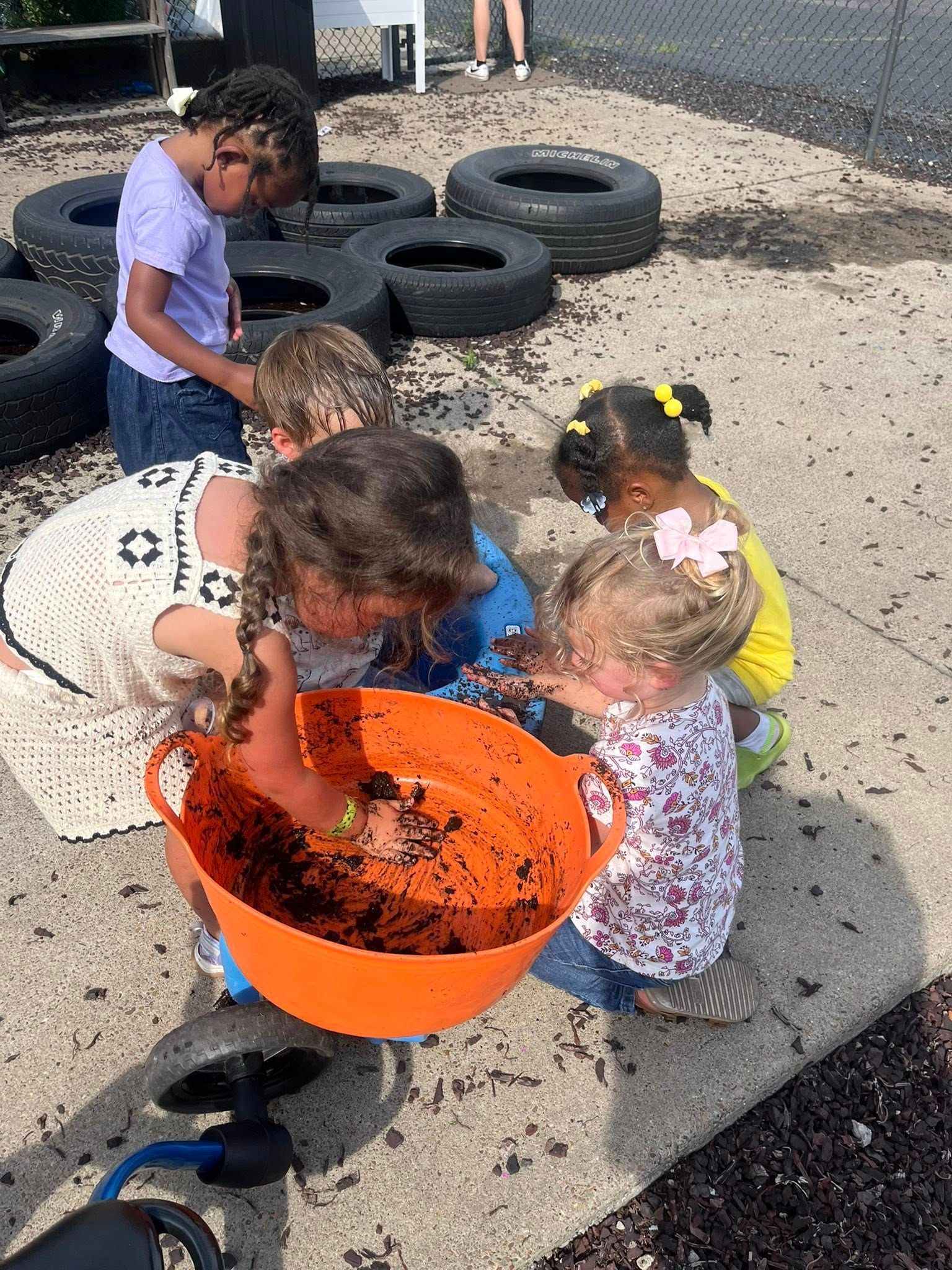 A group of children are playing in the dirt with a large orange bowl.