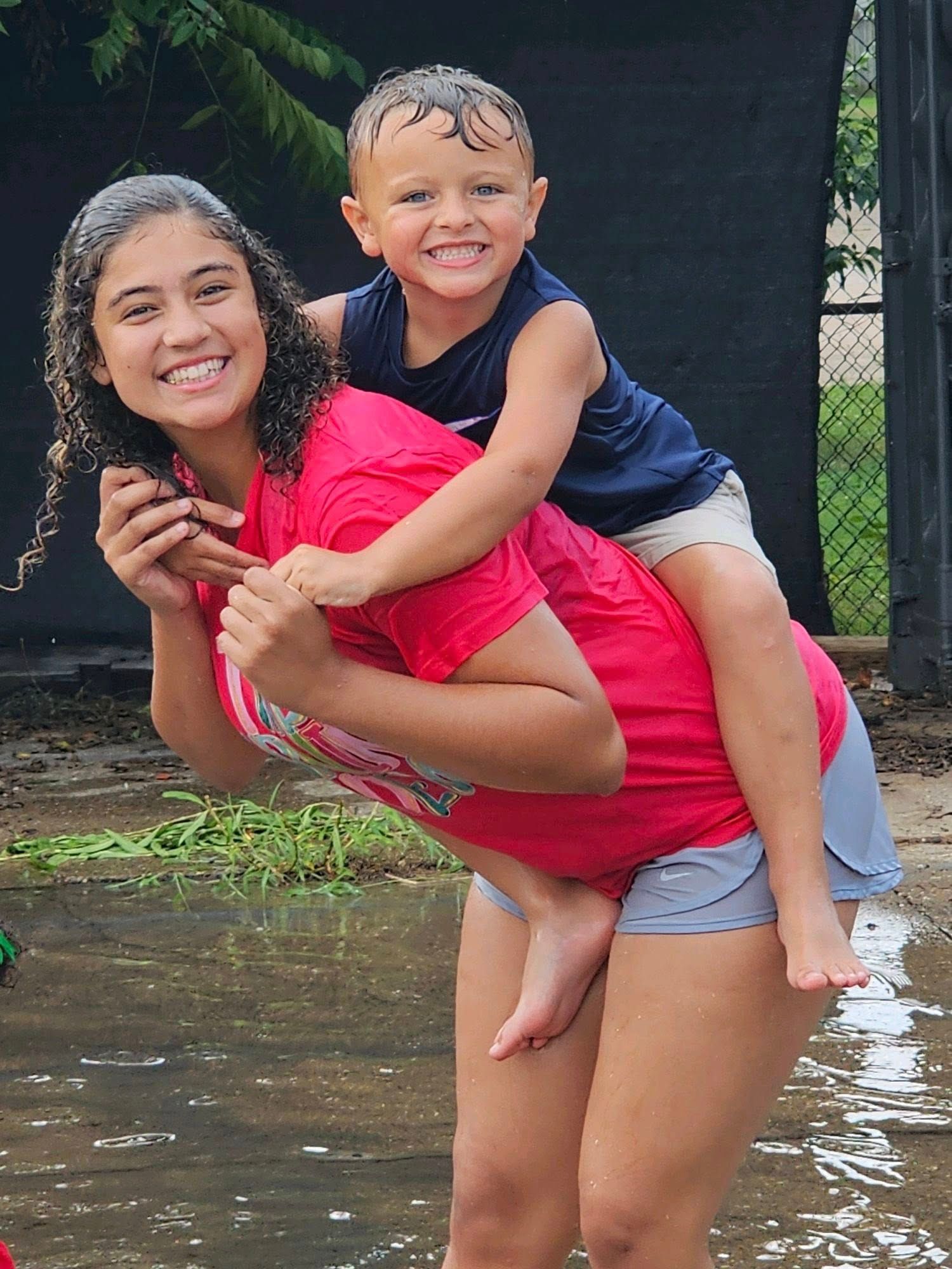 A woman is carrying a child on her back in a puddle of water.