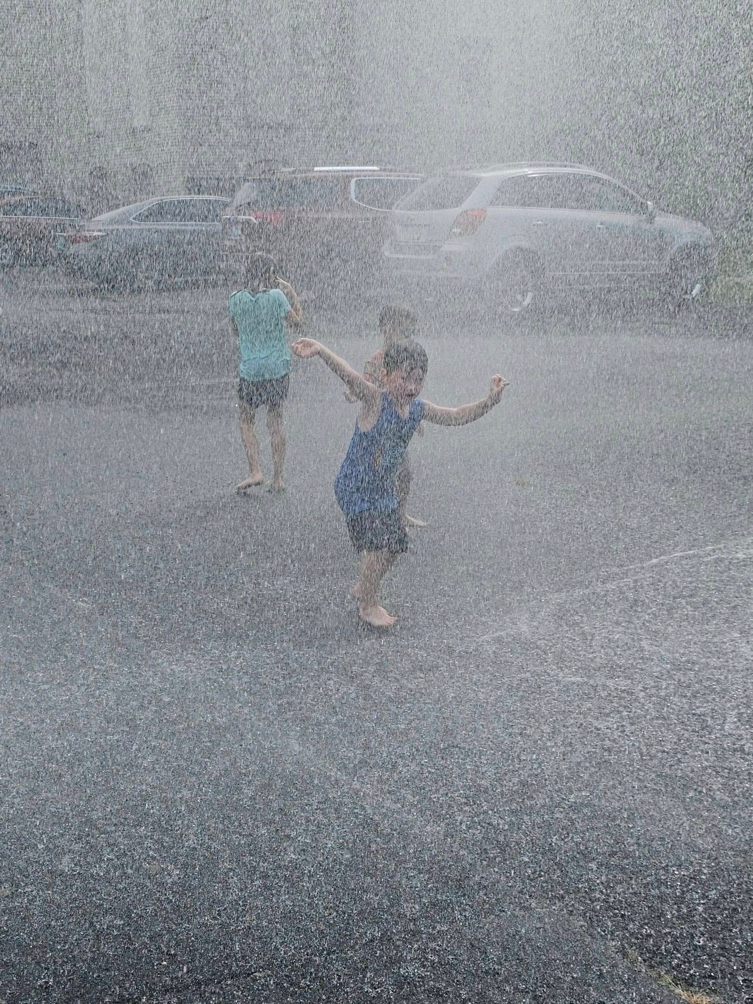 Two children are playing in the rain in a parking lot.