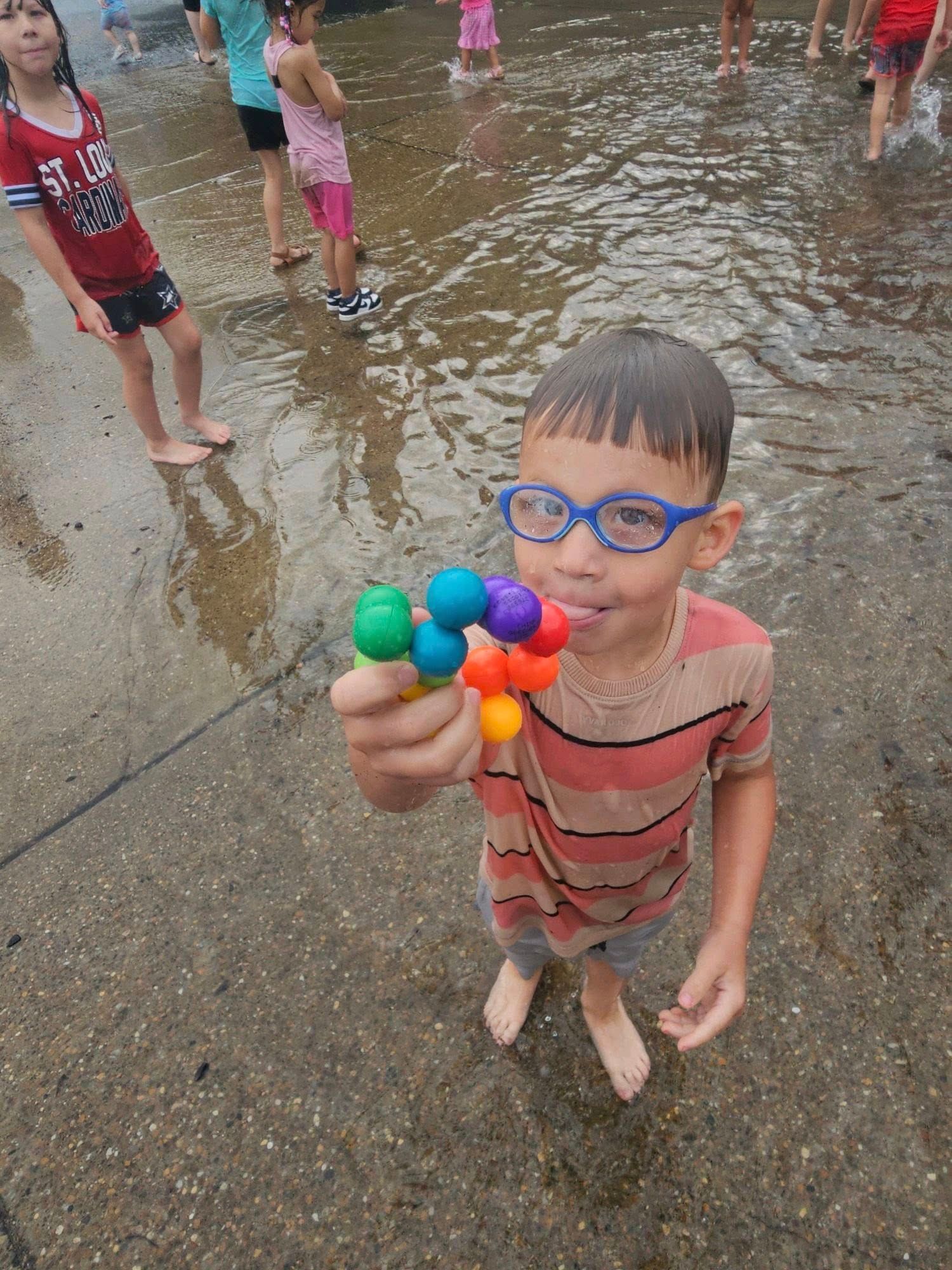 A young boy wearing glasses is holding a toy in a puddle of water.