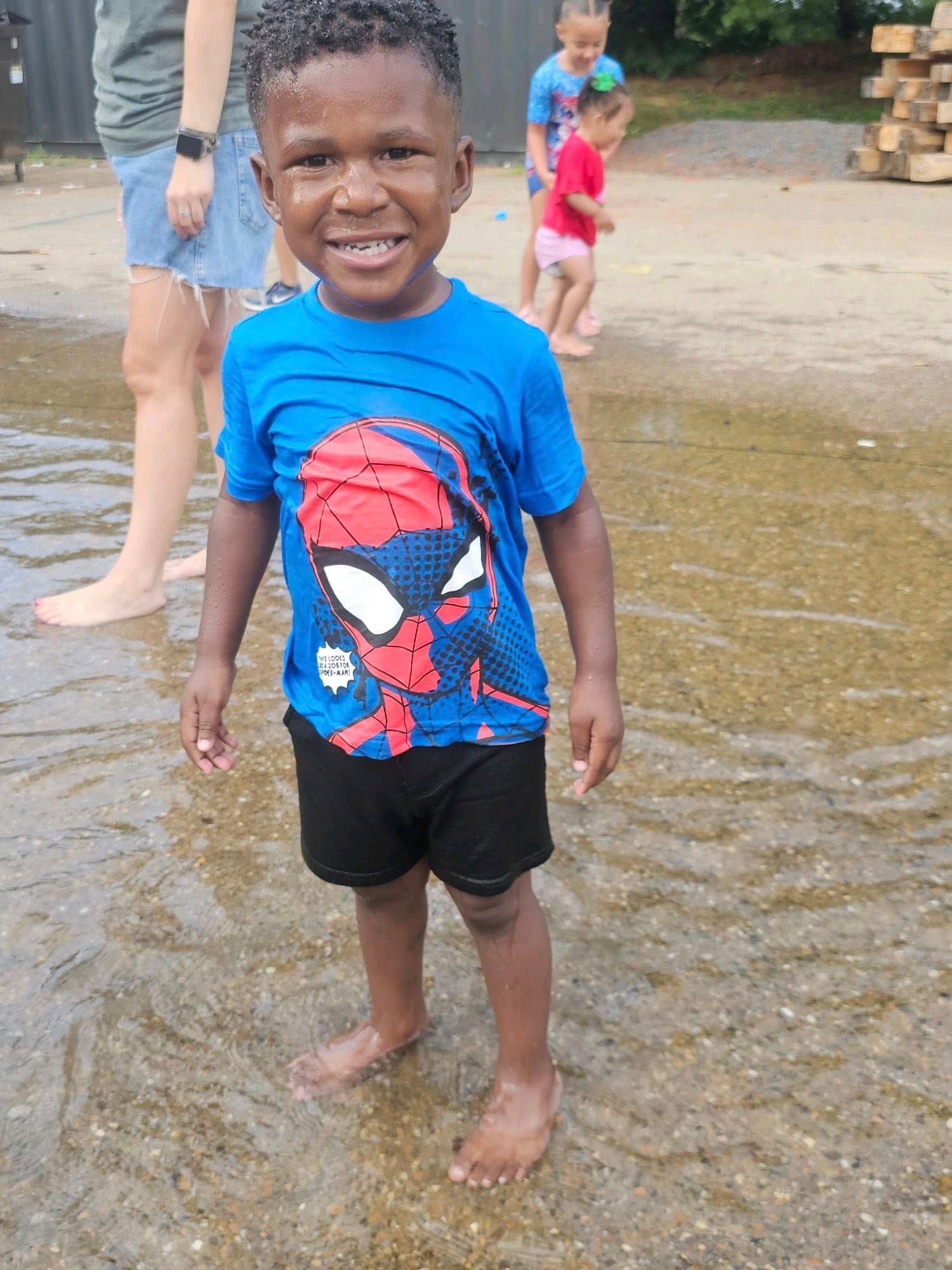A young boy wearing a spiderman shirt is standing in the water.