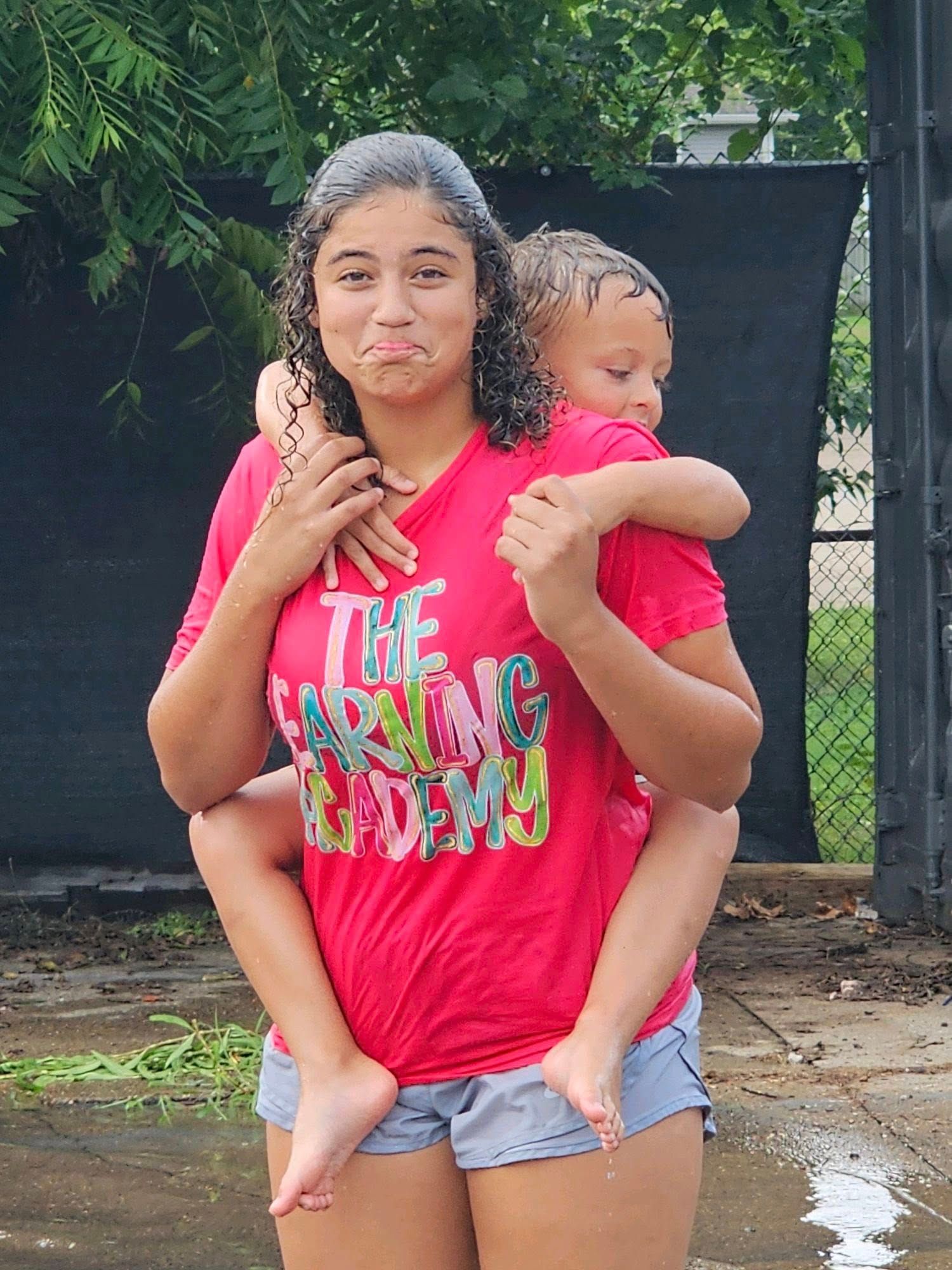 A woman in a red shirt is carrying a child on her back.
