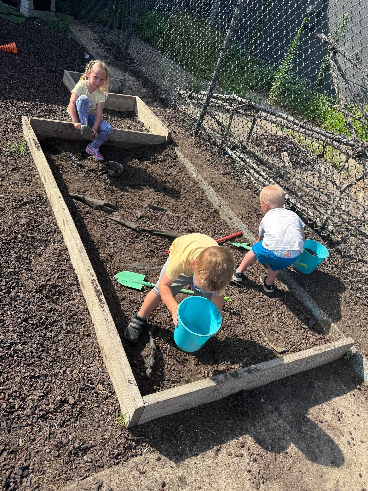Two children are playing in a sandbox with shovels and buckets.