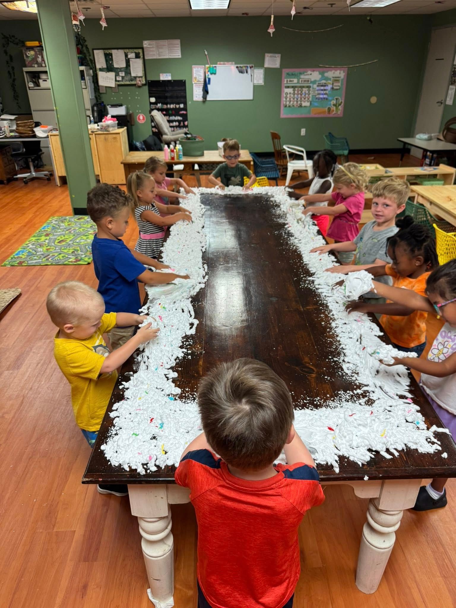 A group of children are playing with foam on a long table.