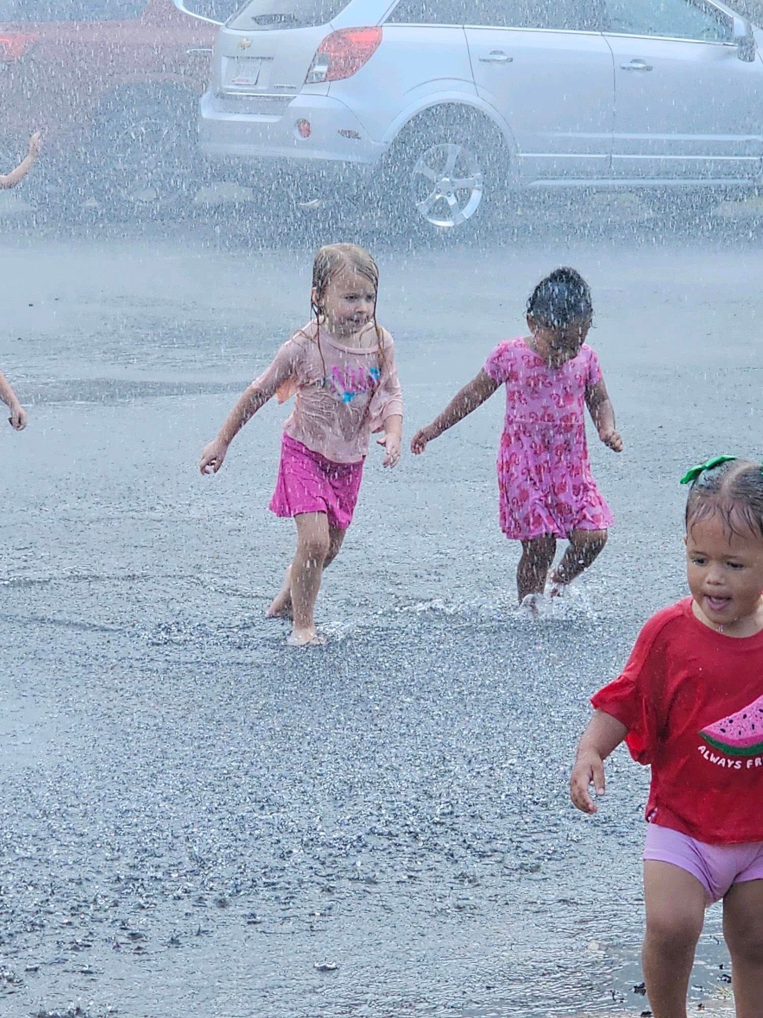 A group of young girls are playing in the rain in a parking lot.