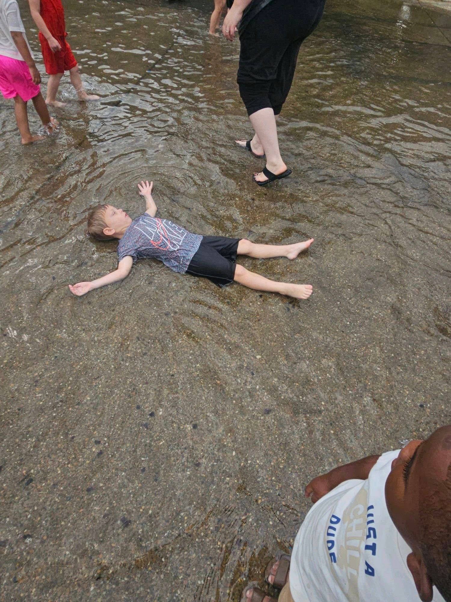A young boy is laying on the ground in a puddle of water.