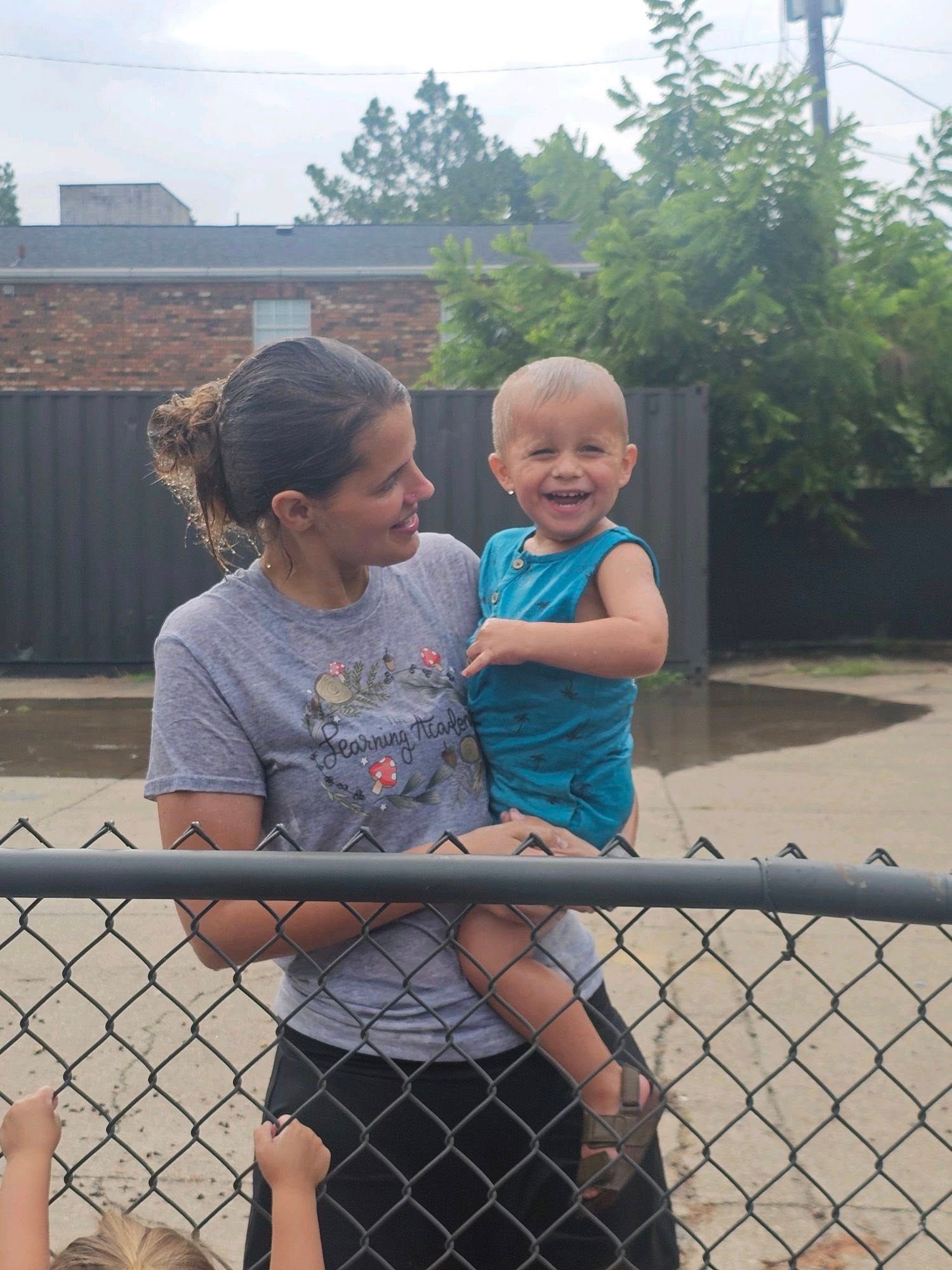A woman is holding a baby in front of a chain link fence