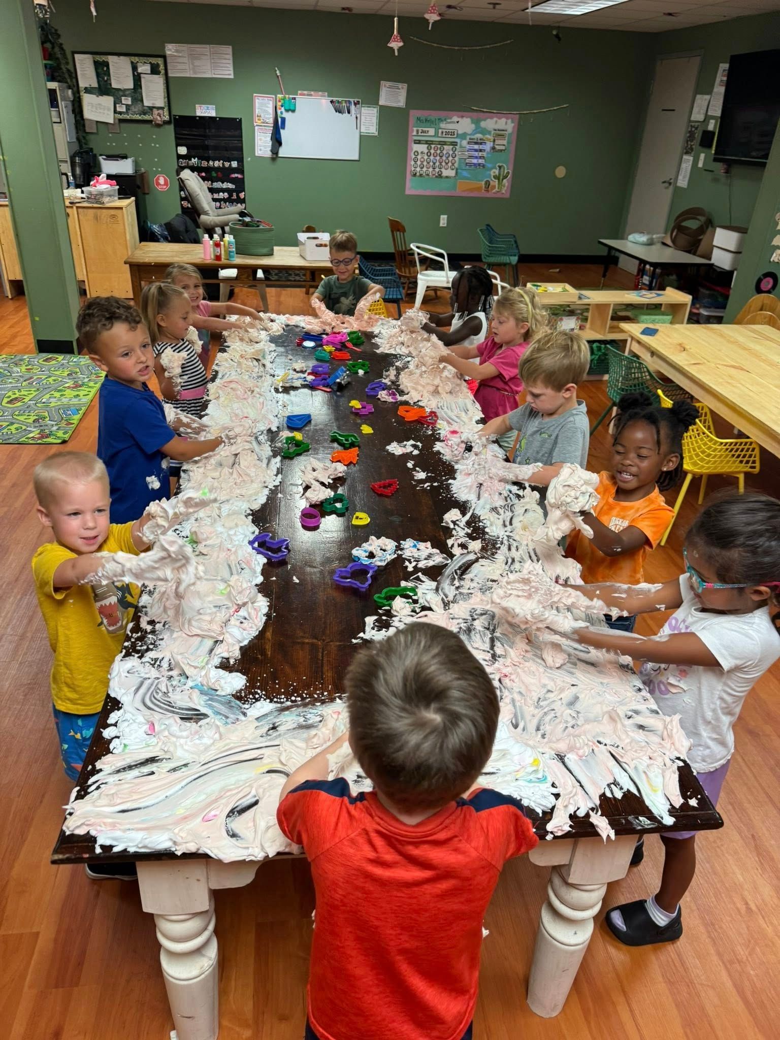A group of children are playing with shaving cream on a long table.