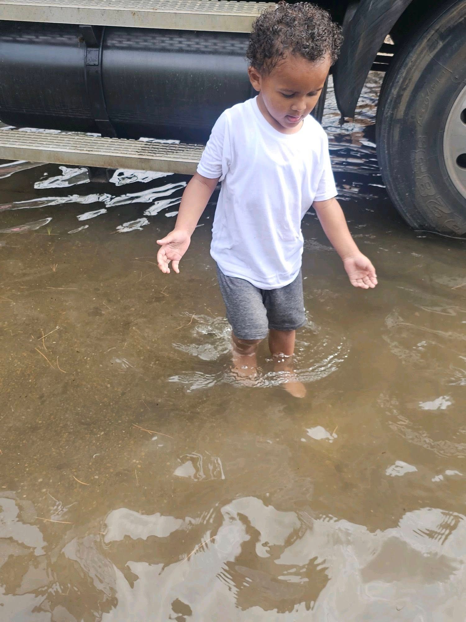 A little boy is standing in a puddle of water next to a truck.