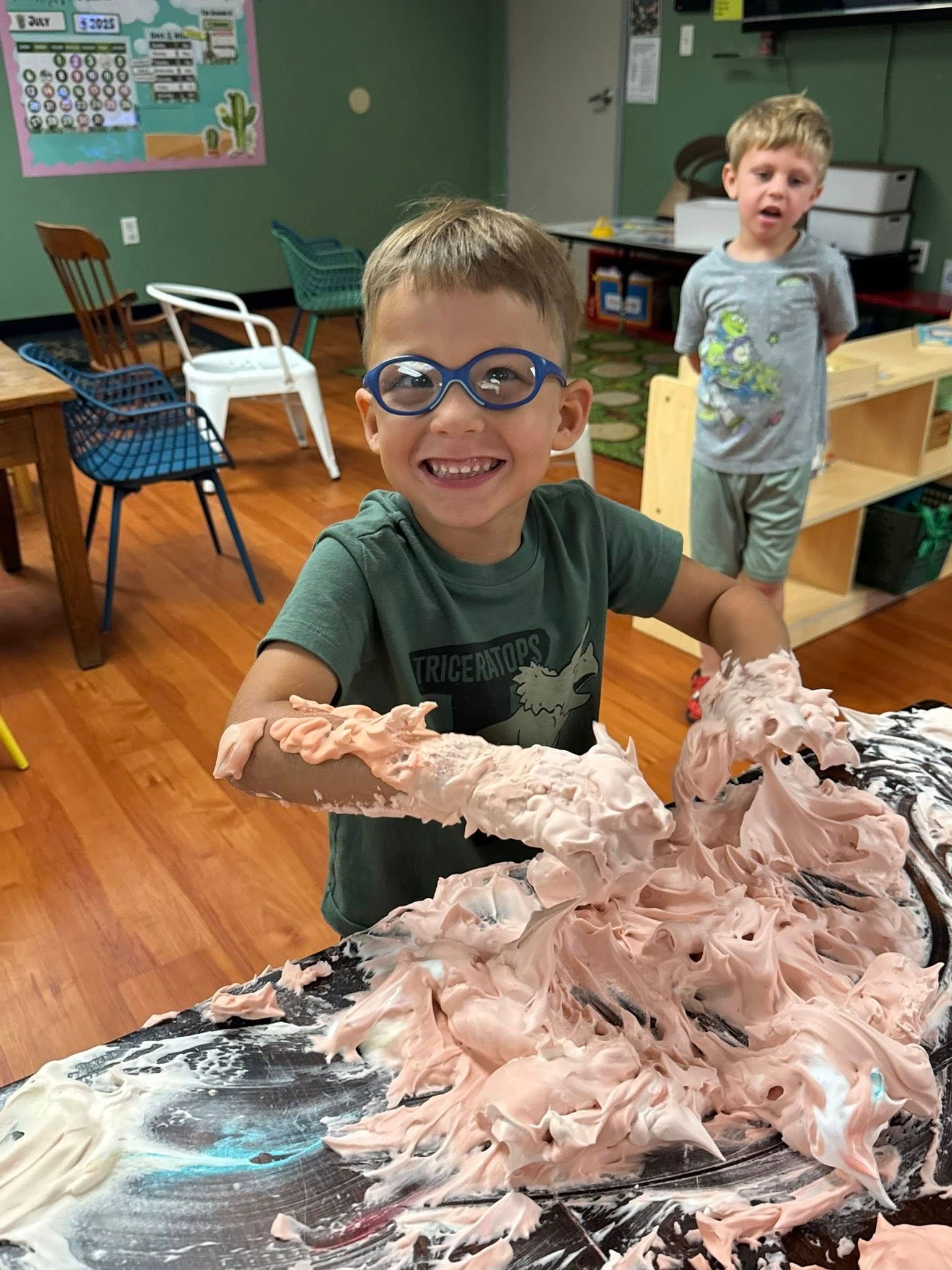 A young boy wearing glasses is playing with foam in a classroom.