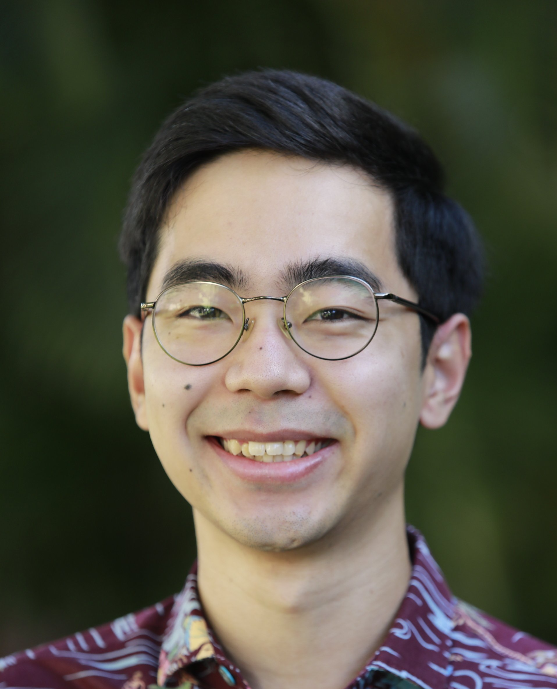 A young man wearing glasses and a purple shirt is smiling for the camera