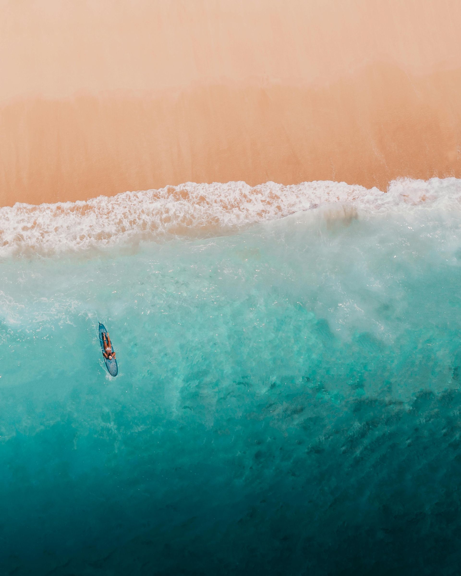 an aerial view of a person riding a wave on a surfboard in the ocean .